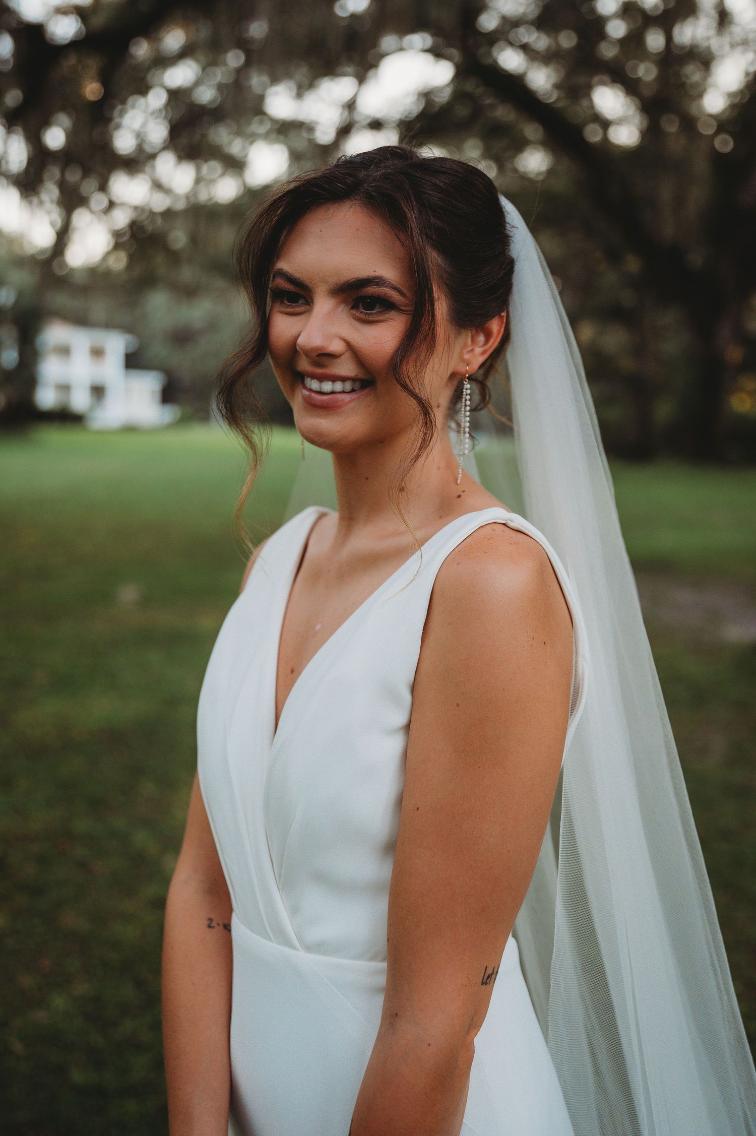 A bride in a classic white V-neck wedding dress and flowing veil smiles outdoors during a Panama City Beach wedding.