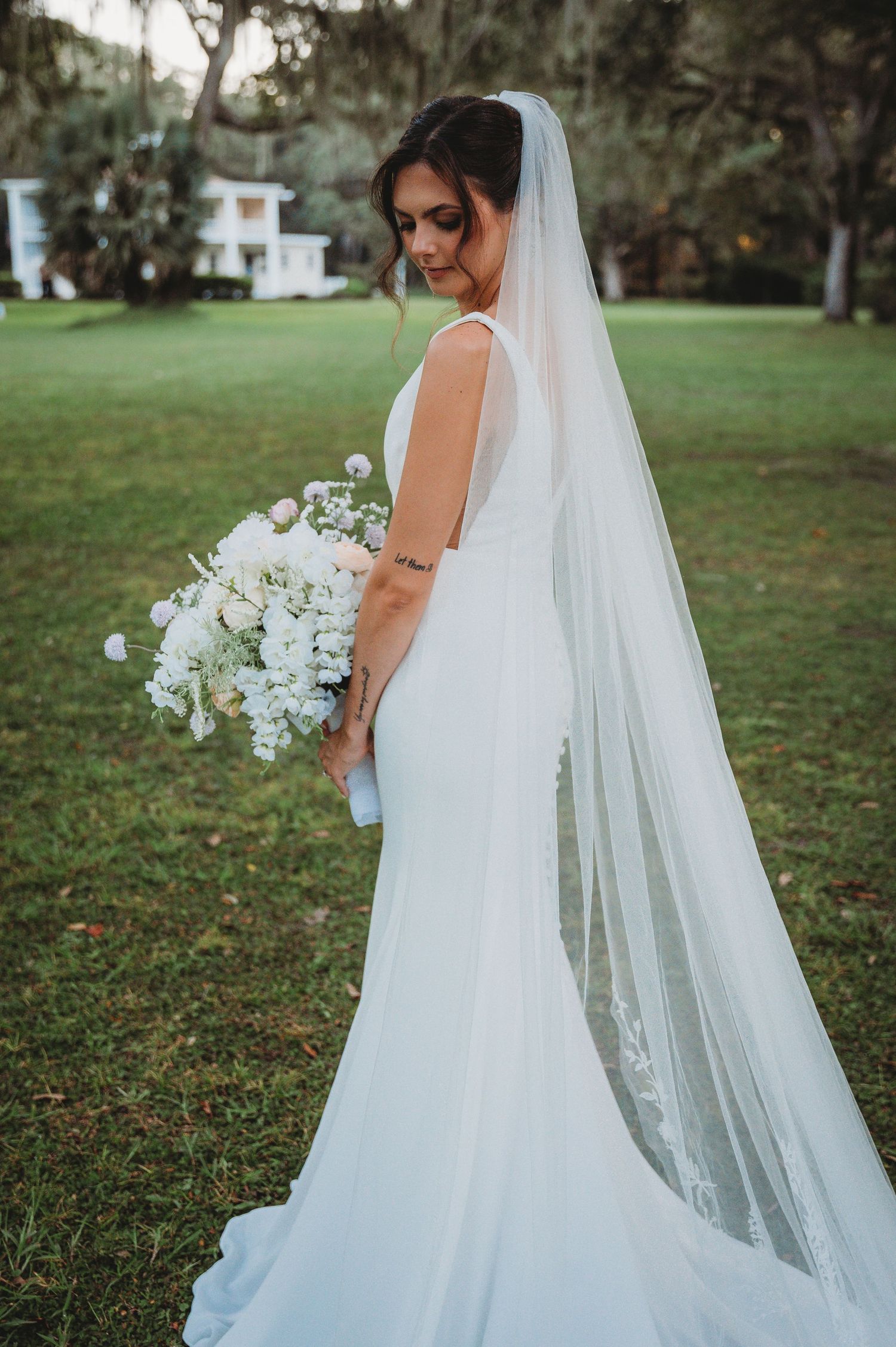 A bride in a flowing white wedding gown and long veil poses in a garden setting during a Panama City Beach wedding.