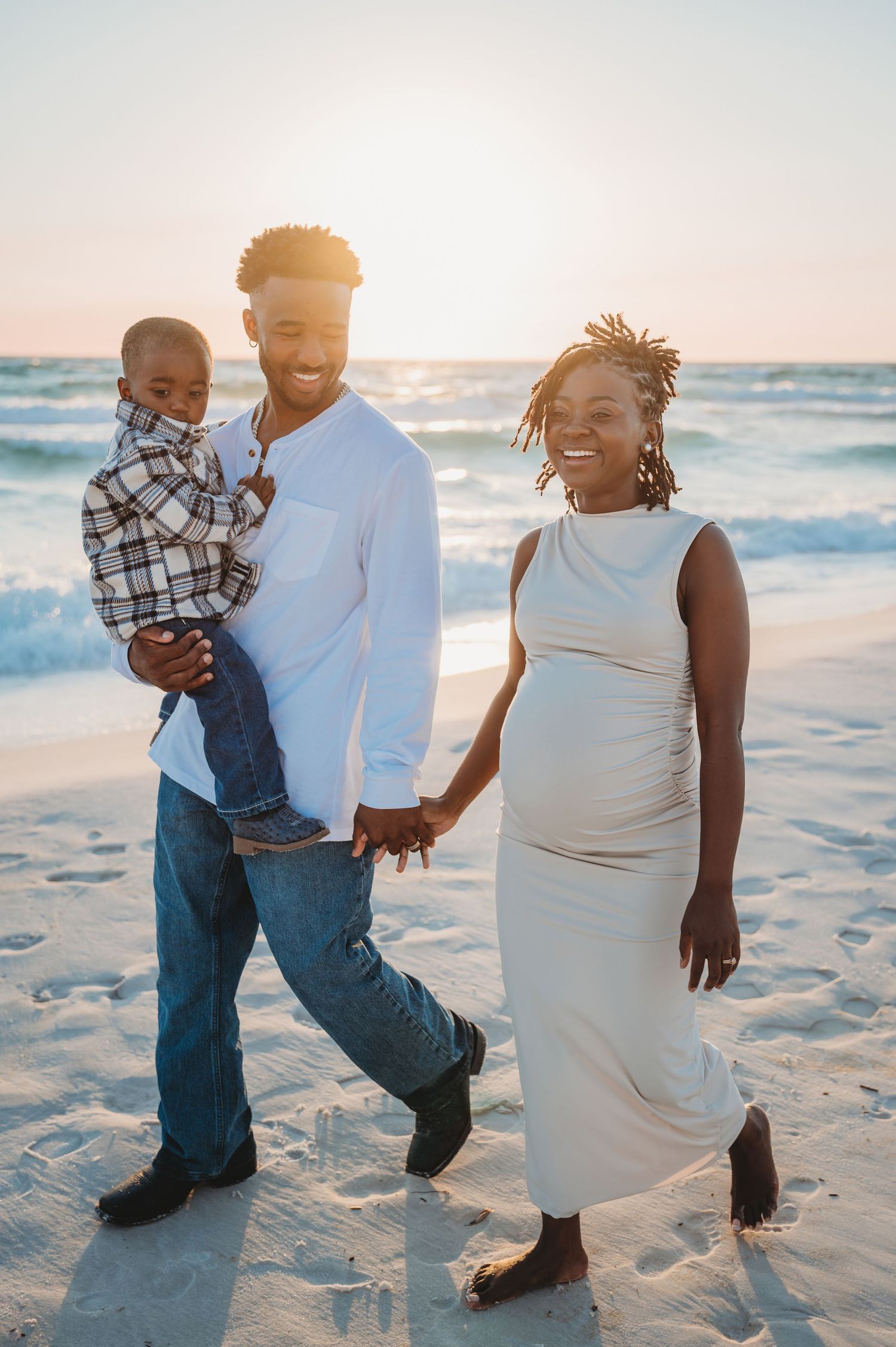 A family enjoys a sunset photoshoot together on a sandy 30A beach with ocean waves in the background.