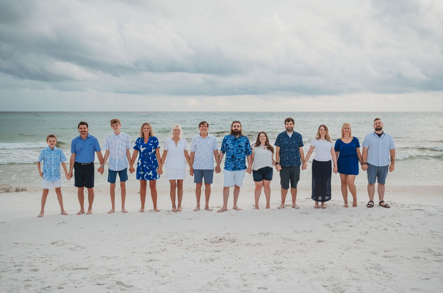 A group of people standing in a line on a white sandy beach with ocean waves and cloudy sky in the background in Panama City Beach.