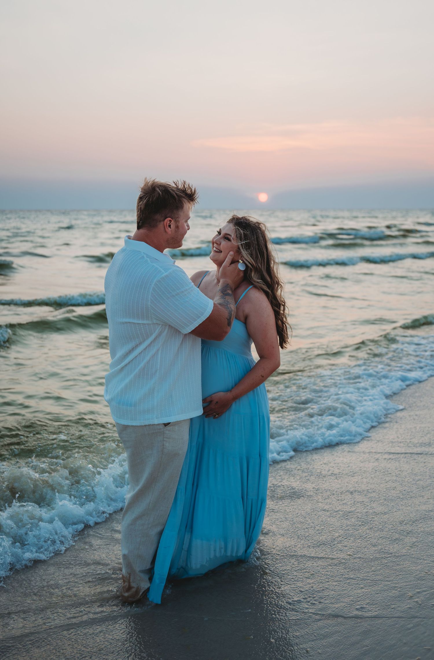 A romantic couple shares intimate moments on the shoreline as waves crash behind them during a maternity session in Laguna Beach.