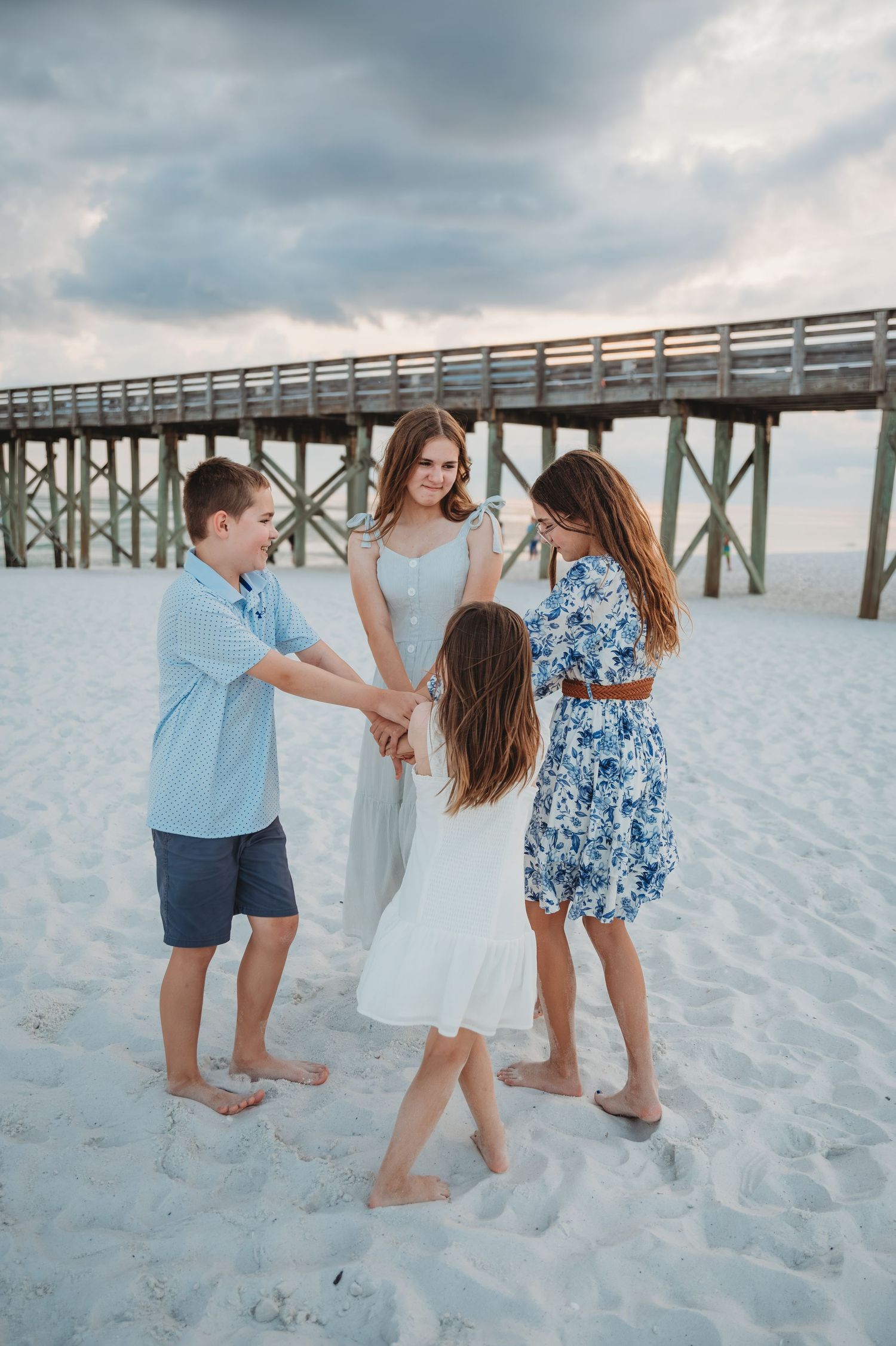 People playfully walking and dancing together on white sandy beach near wooden pier during sunset in Panama City Beach.