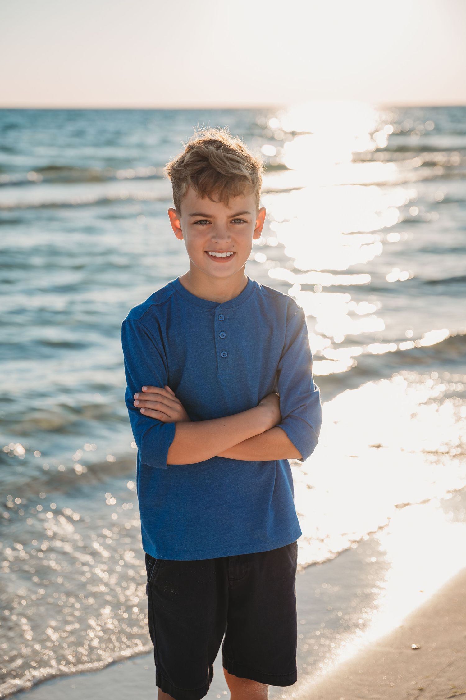 A child in a blue shirt stands on a sunny Panama City Beach with sparkling ocean waves in the background.