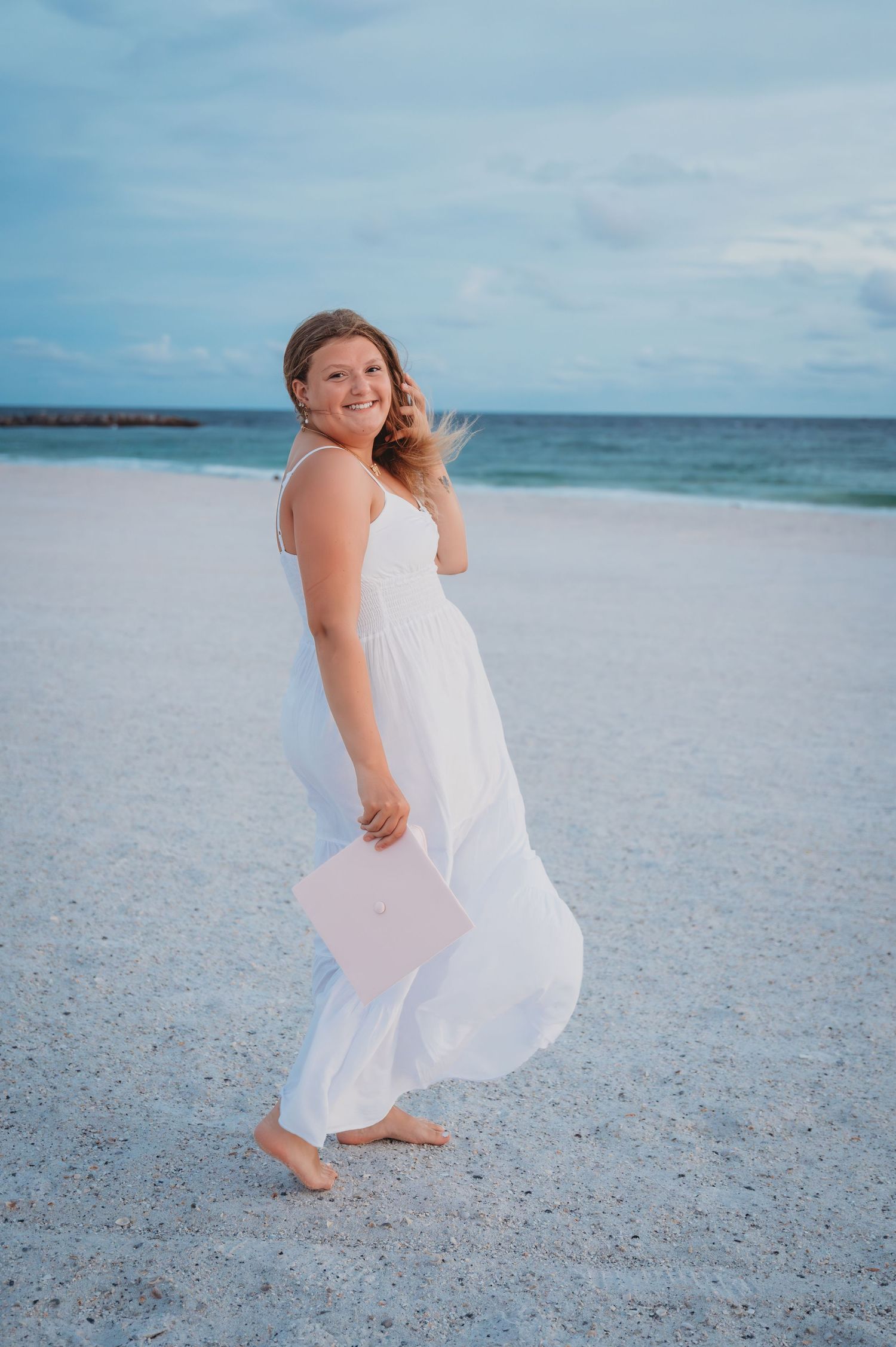 A senior in a flowing white dress dances gracefully on a pristine beach with turquoise waters and blue sky in the background in Panama City.