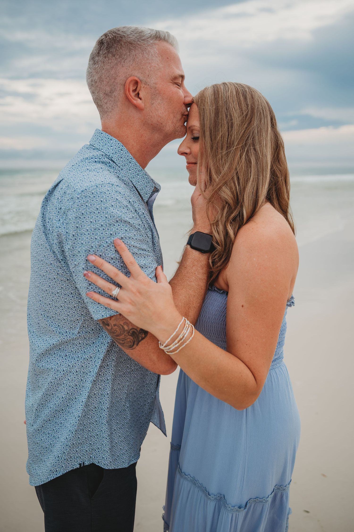 Couple sharing romantic moments together at the beach during sunset wearing blue and light blue outfits in Panama City Beach.