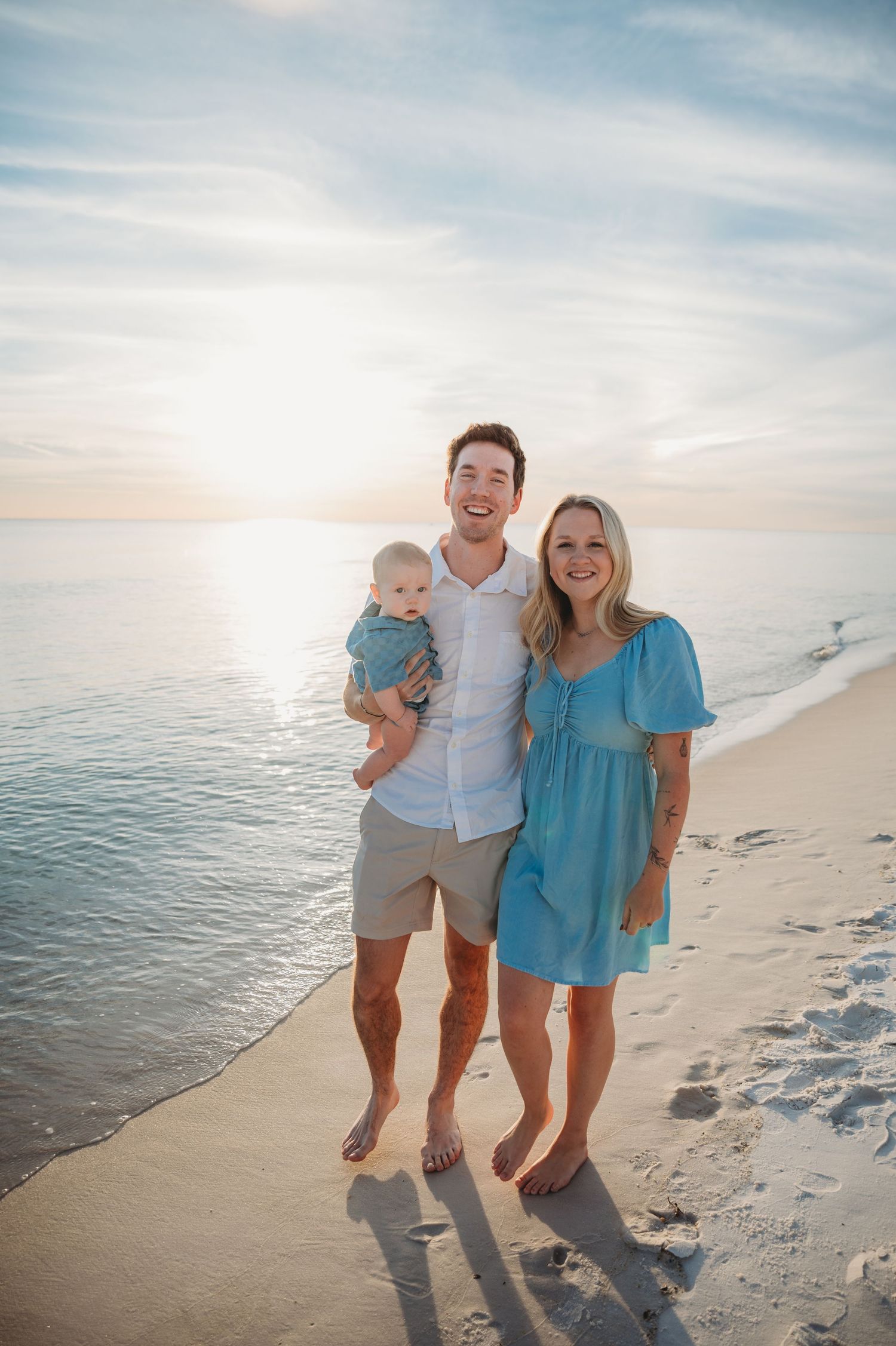 A family enjoys a sunset stroll together along a Emerald Coast beach with calm ocean waters in the background.