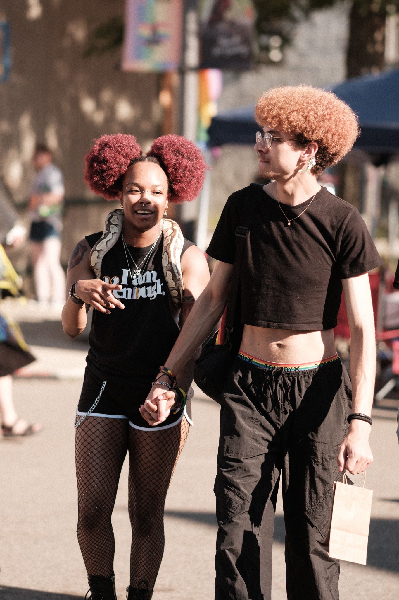Two people with vibrant curly hairstyles walk together at an outdoor festival.