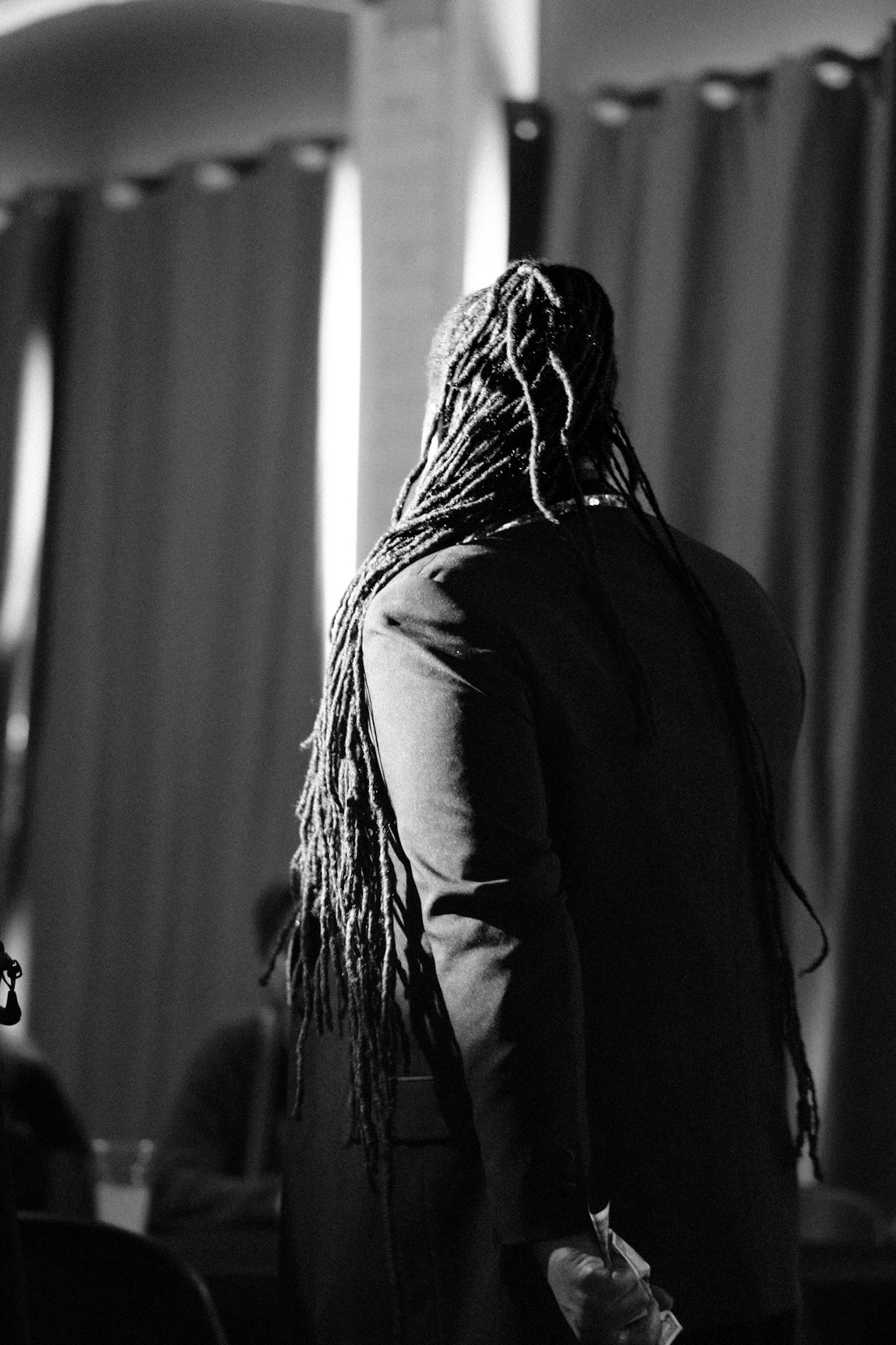 Back view of person with long braided hair against curtained background.