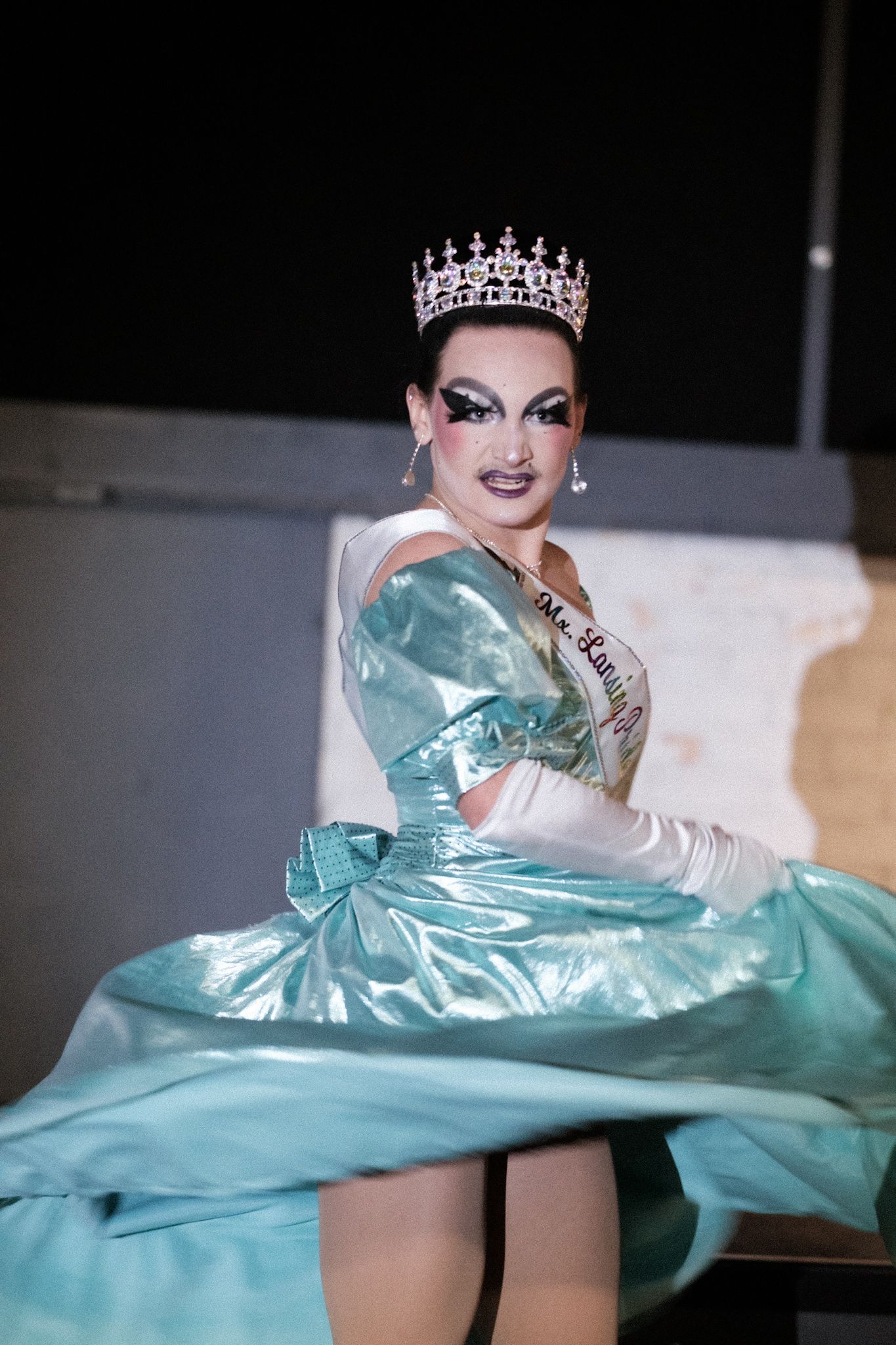 Performer in mint green gown and crown poses dramatically with flowing fabric movement during glamorous photoshoot.