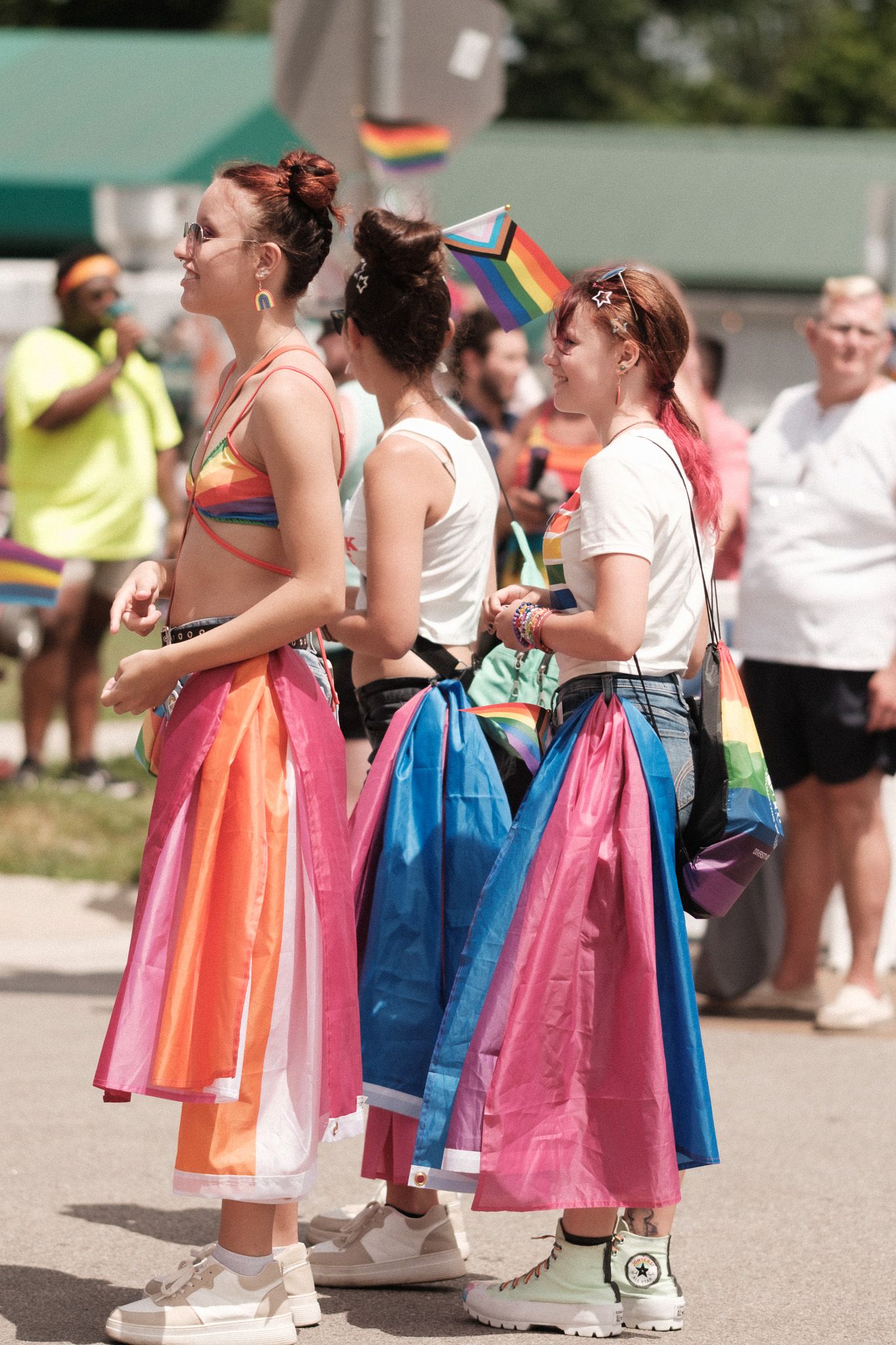 Three people wearing colorful rainbow-inspired skirts stand together at a Pride festival celebration.