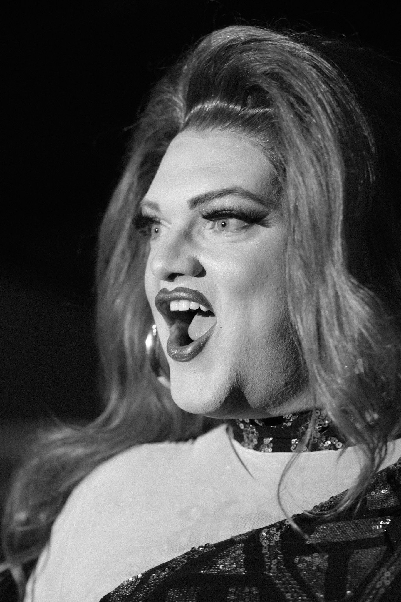 Dramatic black and white portrait of performer with bold makeup and choker necklace.