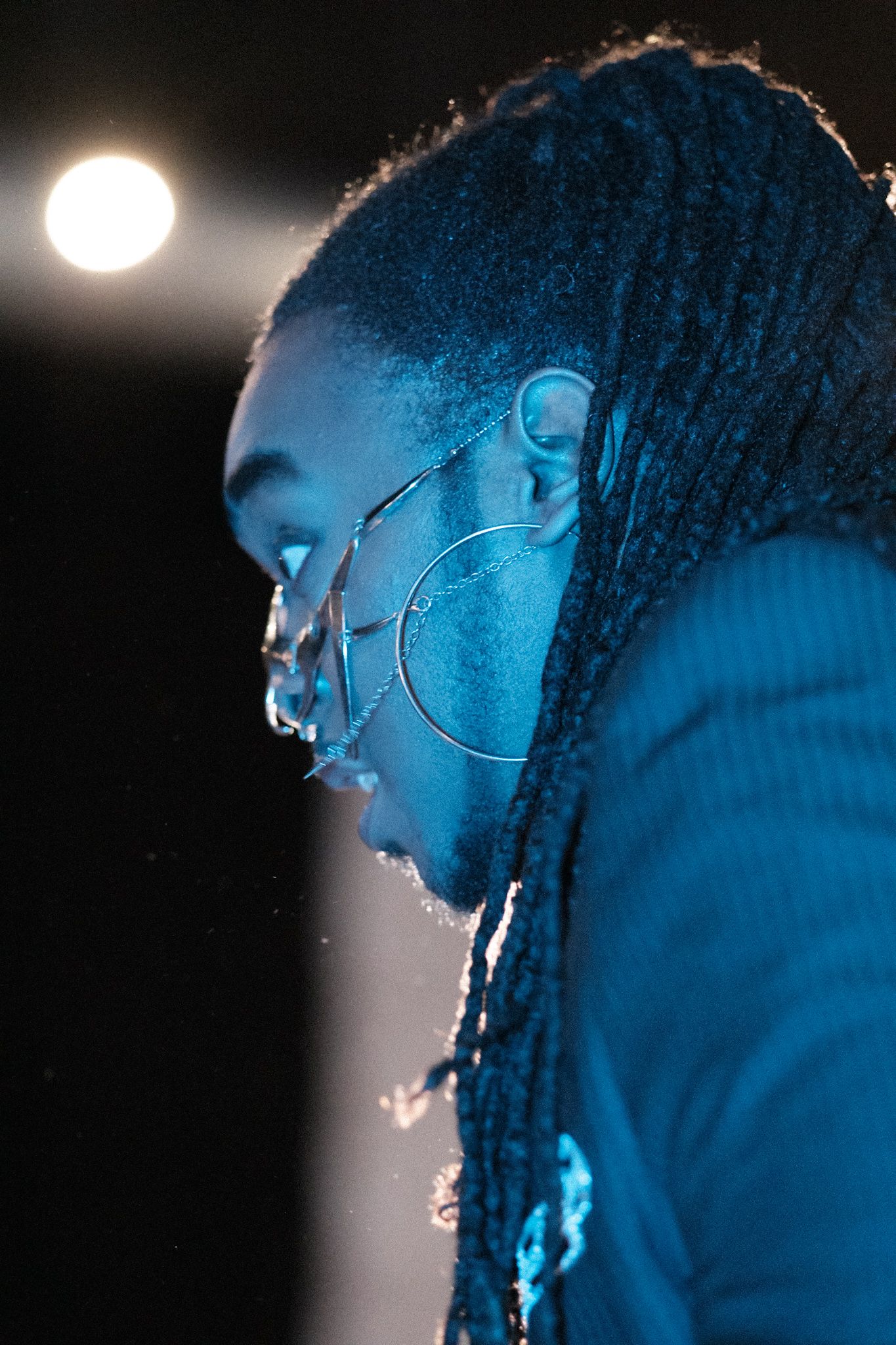 Profile silhouette with blue lighting and large hoop earrings against dark background.