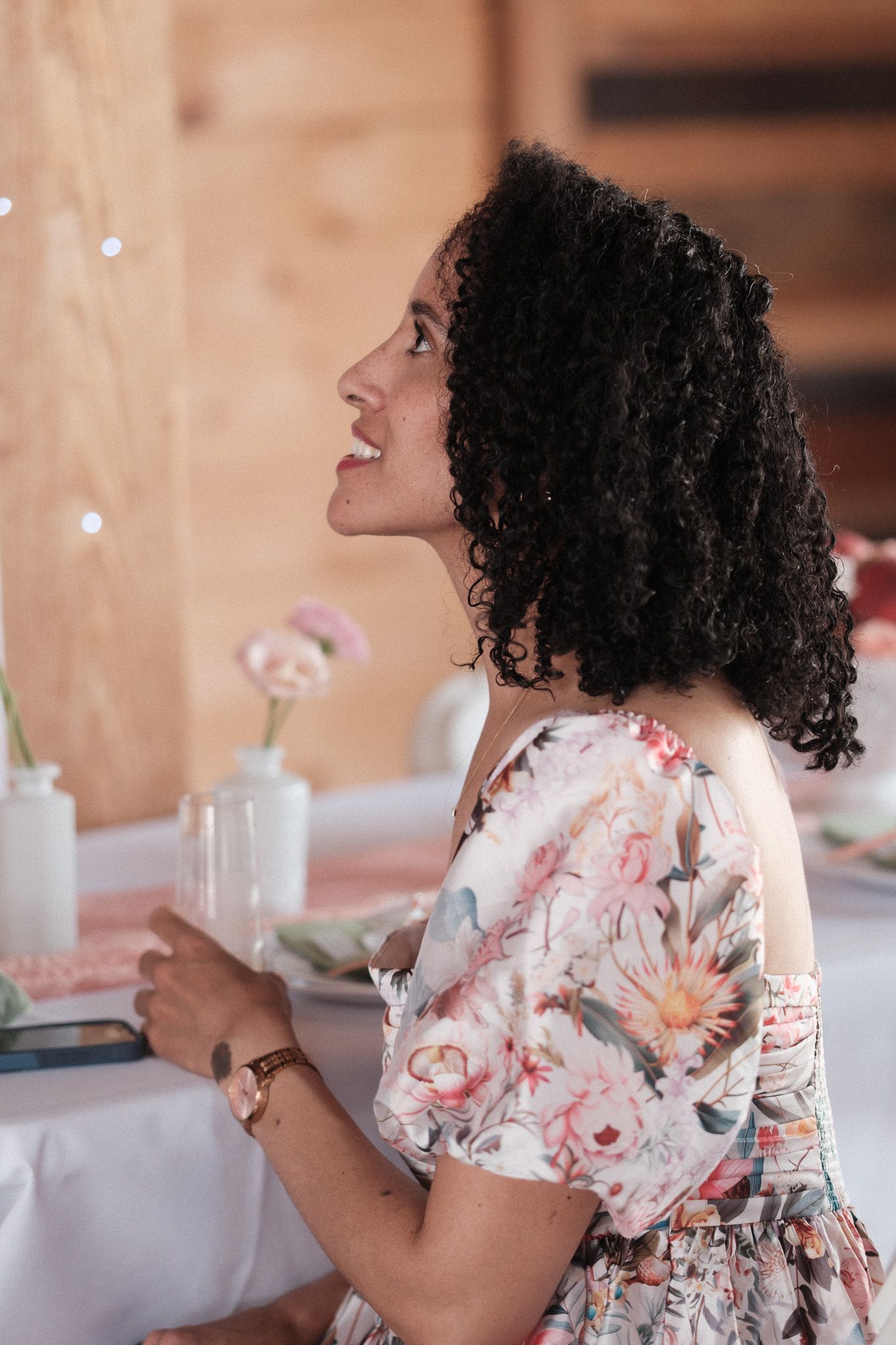 A joyful guest in a floral dress sits at an elegantly decorated table at a special event.