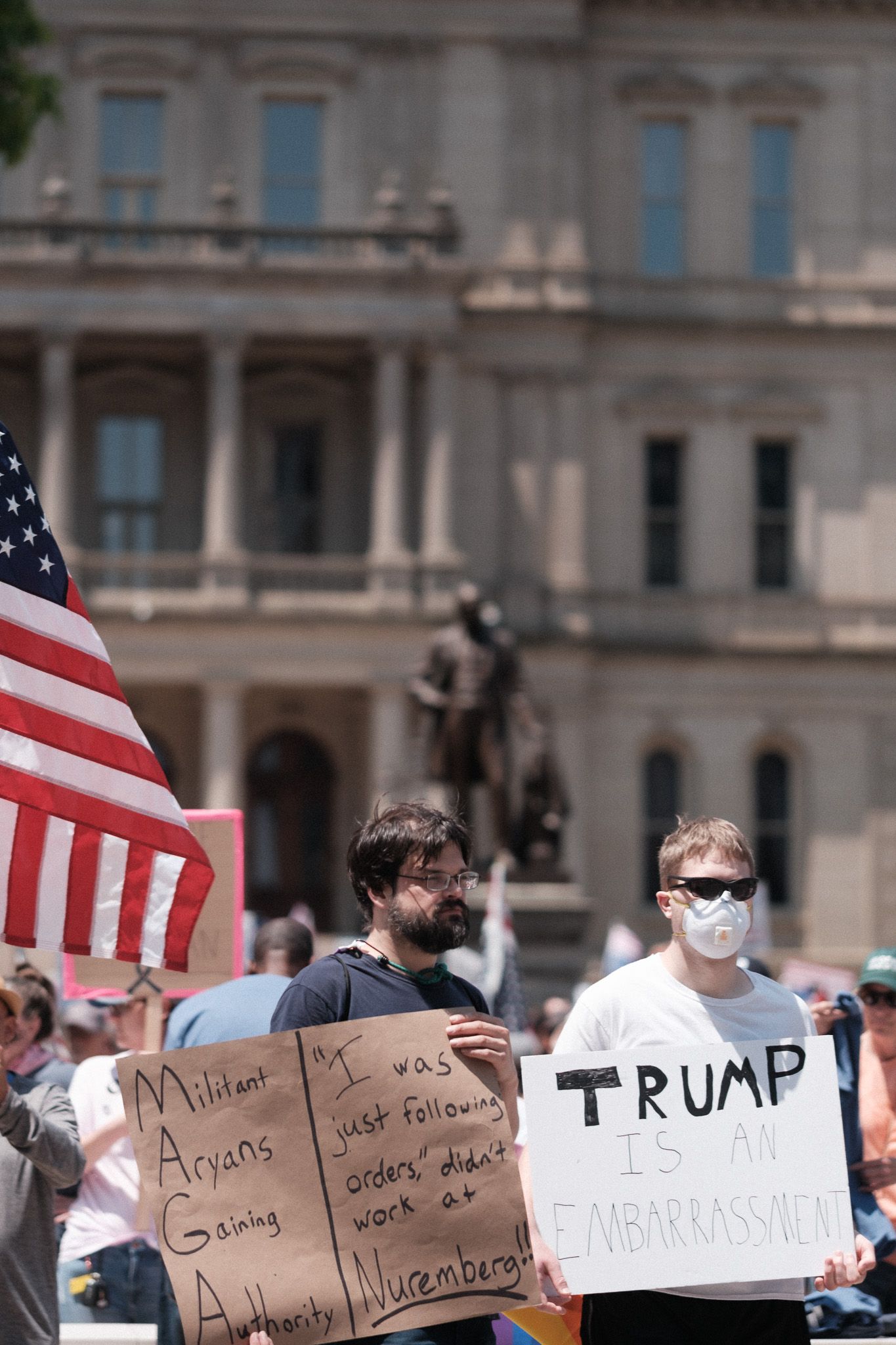 Protesters holding signs and American flags outside a government building during a demonstration.