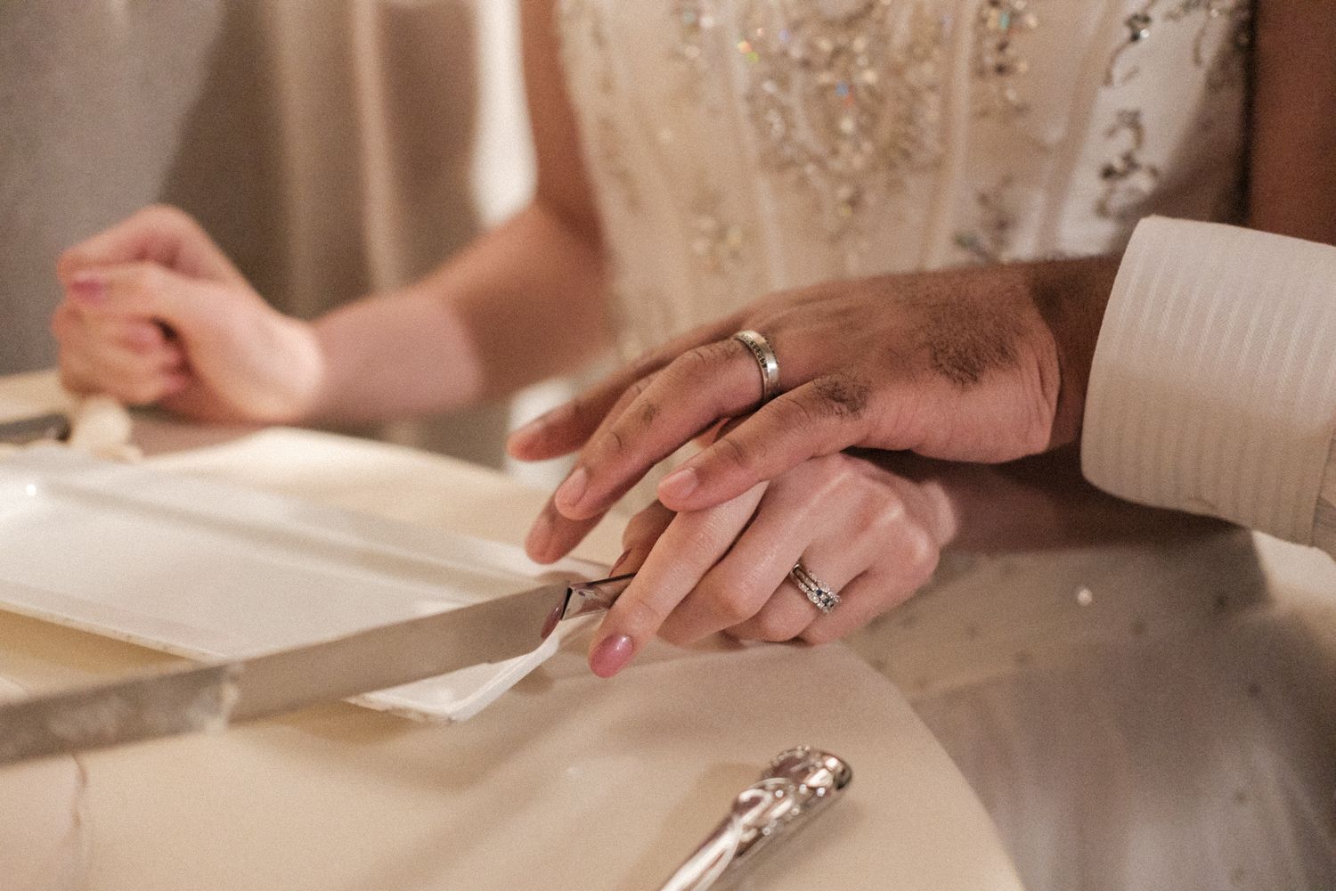 Two hands wearing wedding rings rest together on a table, symbolizing marriage and commitment.