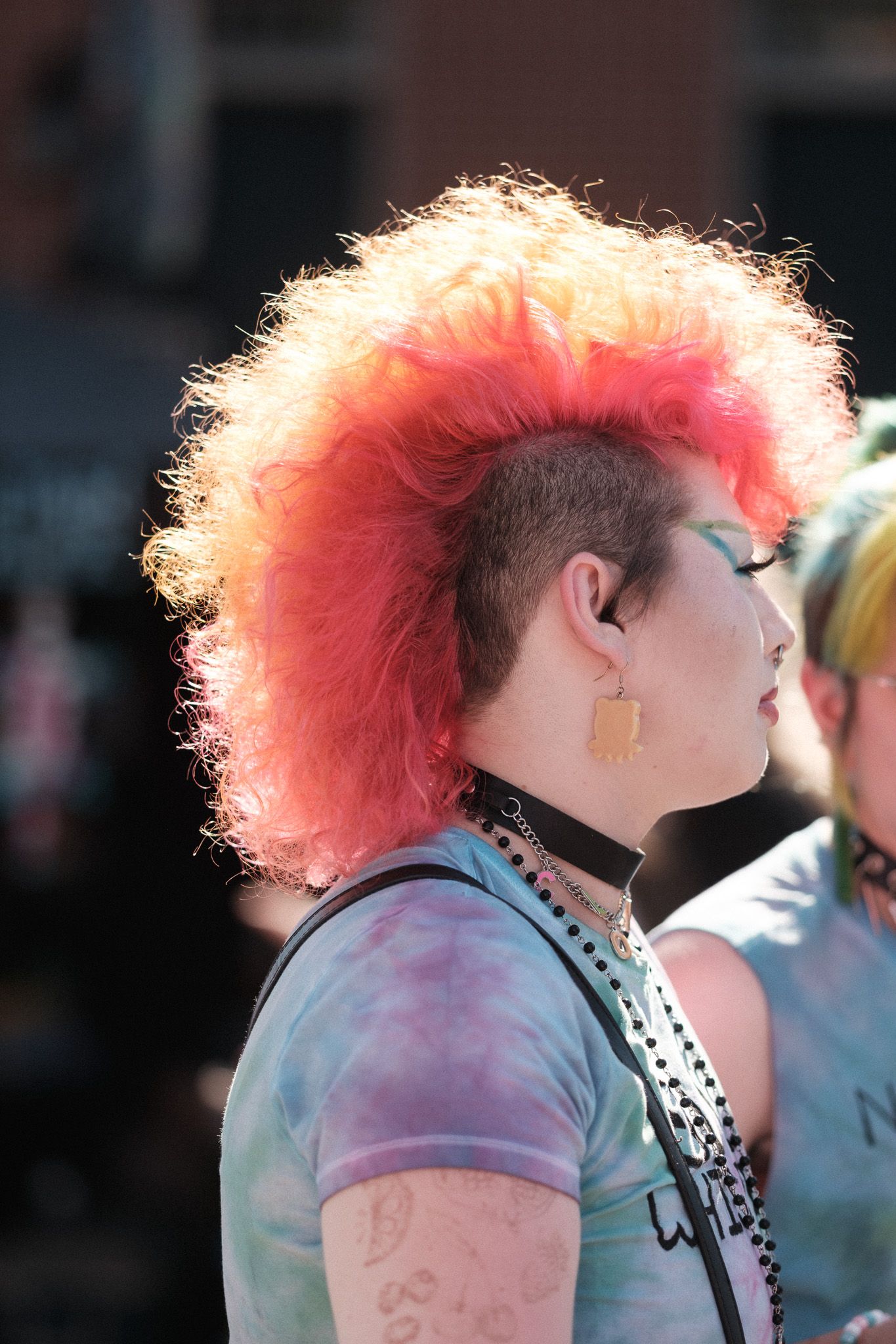 A punk-styled person with bright pink mohawk hairstyle and tie-dye shirt.