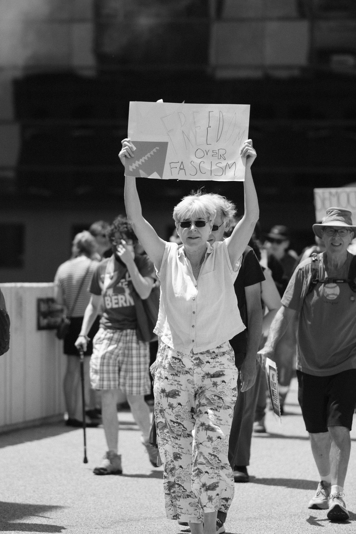 A protester in camouflage pants holds up a sign at an outdoor demonstration.