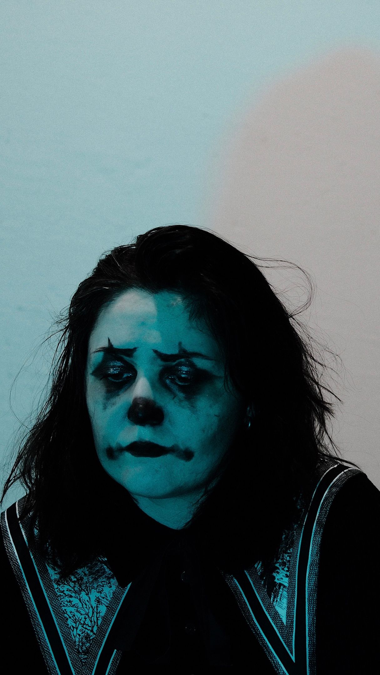 A dramatic portrait with turquoise lighting shows a person wearing dark makeup and a leather jacket against a light background.