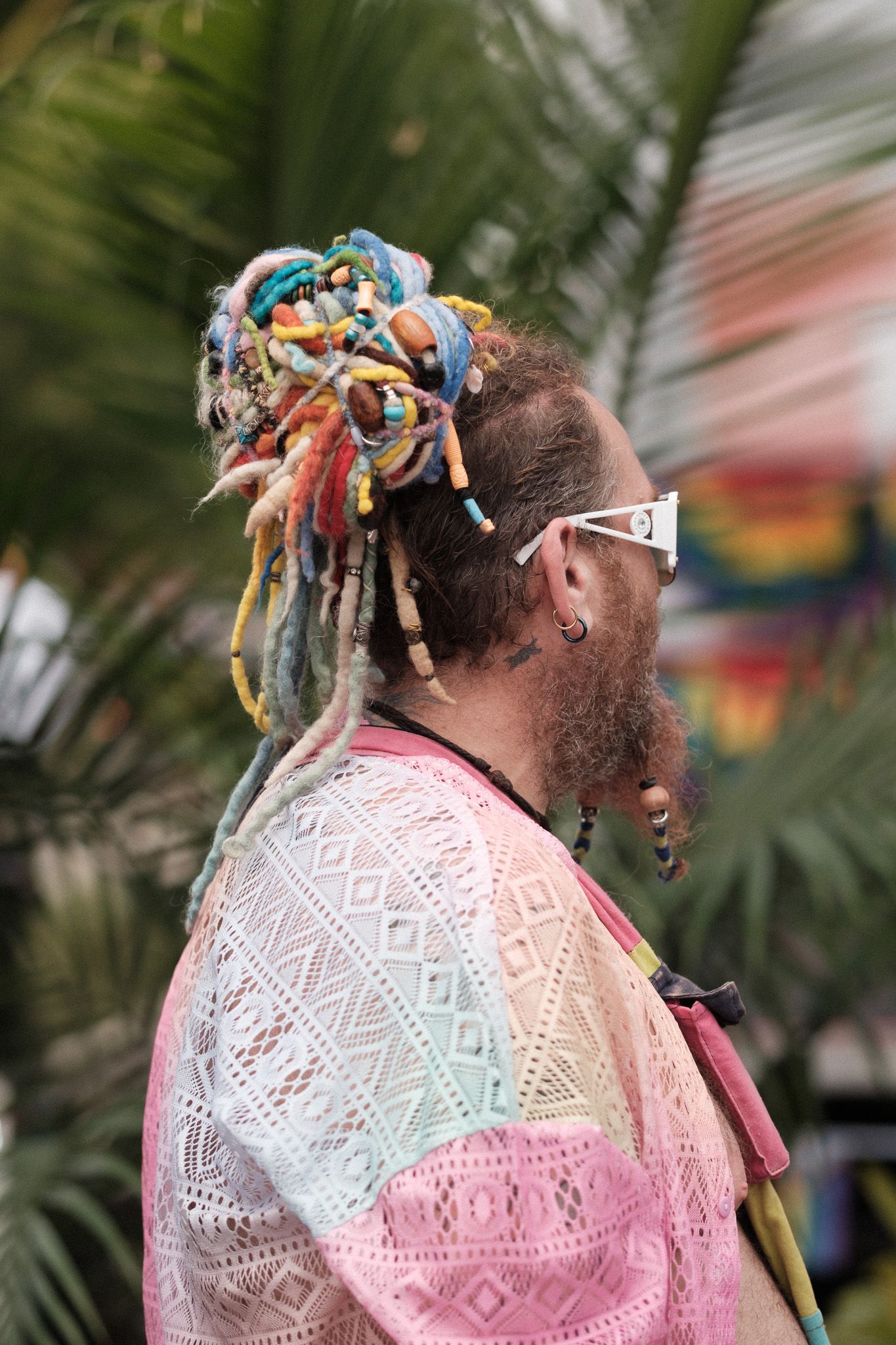 A colorful festival-goer wearing a pastel geometric pattern shirt and ornate hair decorations.