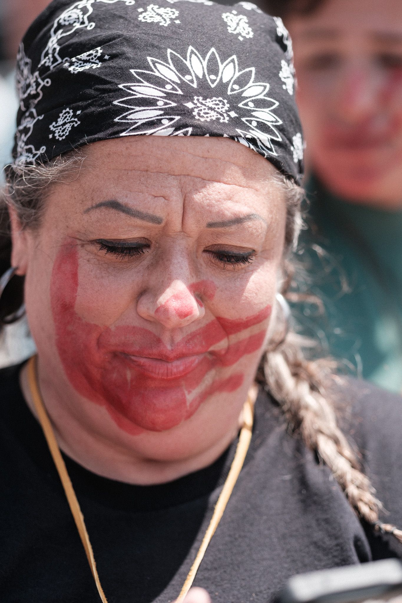 A person wearing a black bandana with white designs and red face paint at a protest rally.