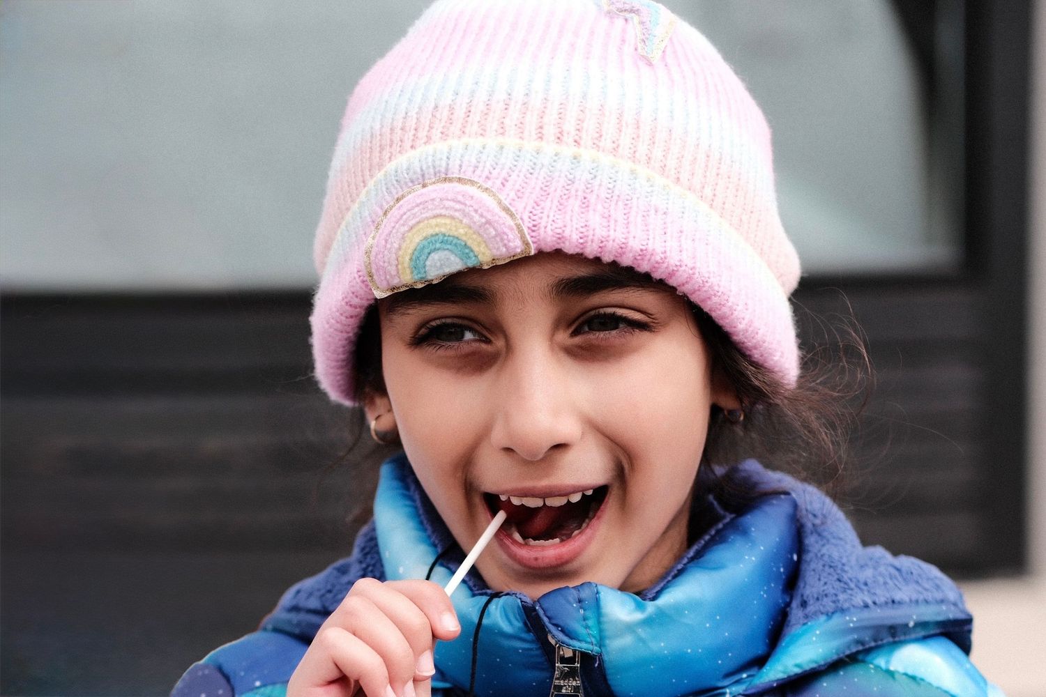 Child in a pink winter hat and blue coat smiling and laughing in sequence.