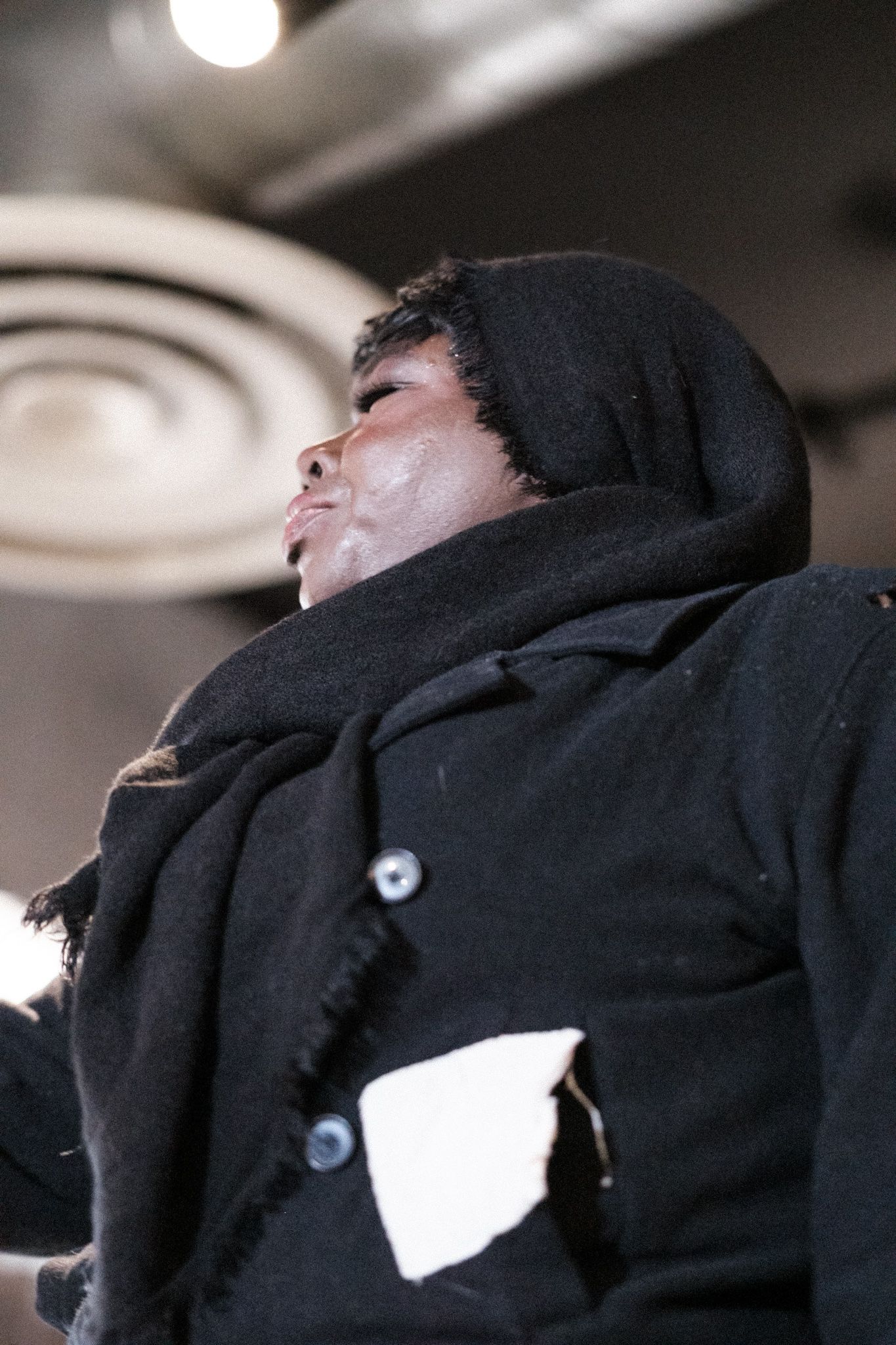 Performer in black hooded coat captured in dramatic profile lighting.