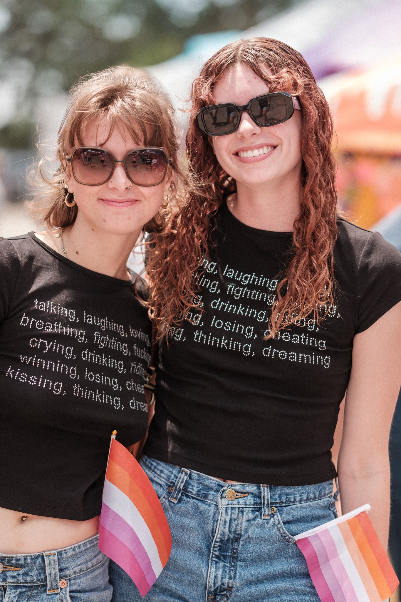 Two people wearing black crop tops with text and denim shorts at a festival.
