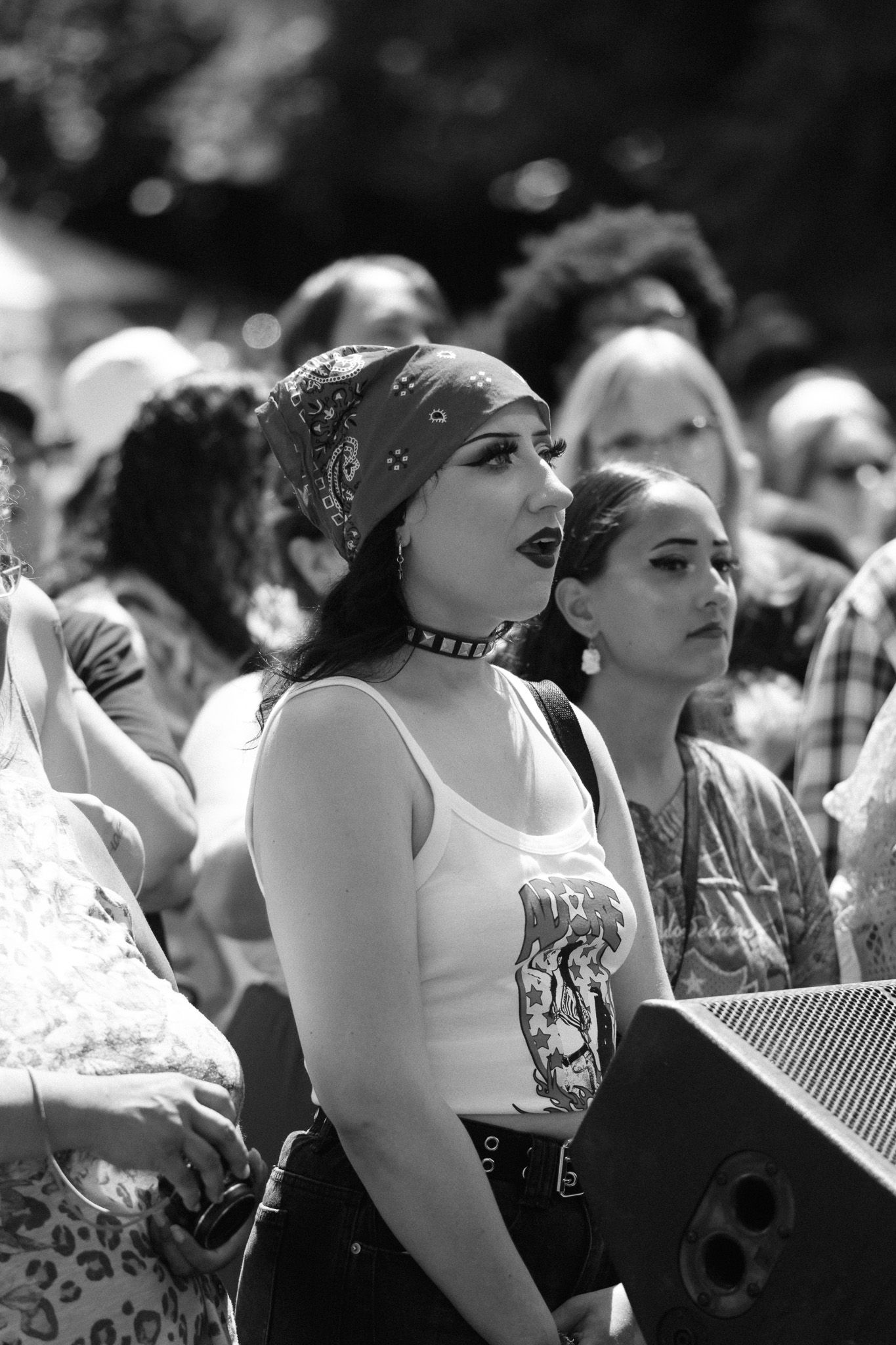 Black and white photo of a crowd at an outdoor event, with a woman wearing a bandana and tank top in focus.