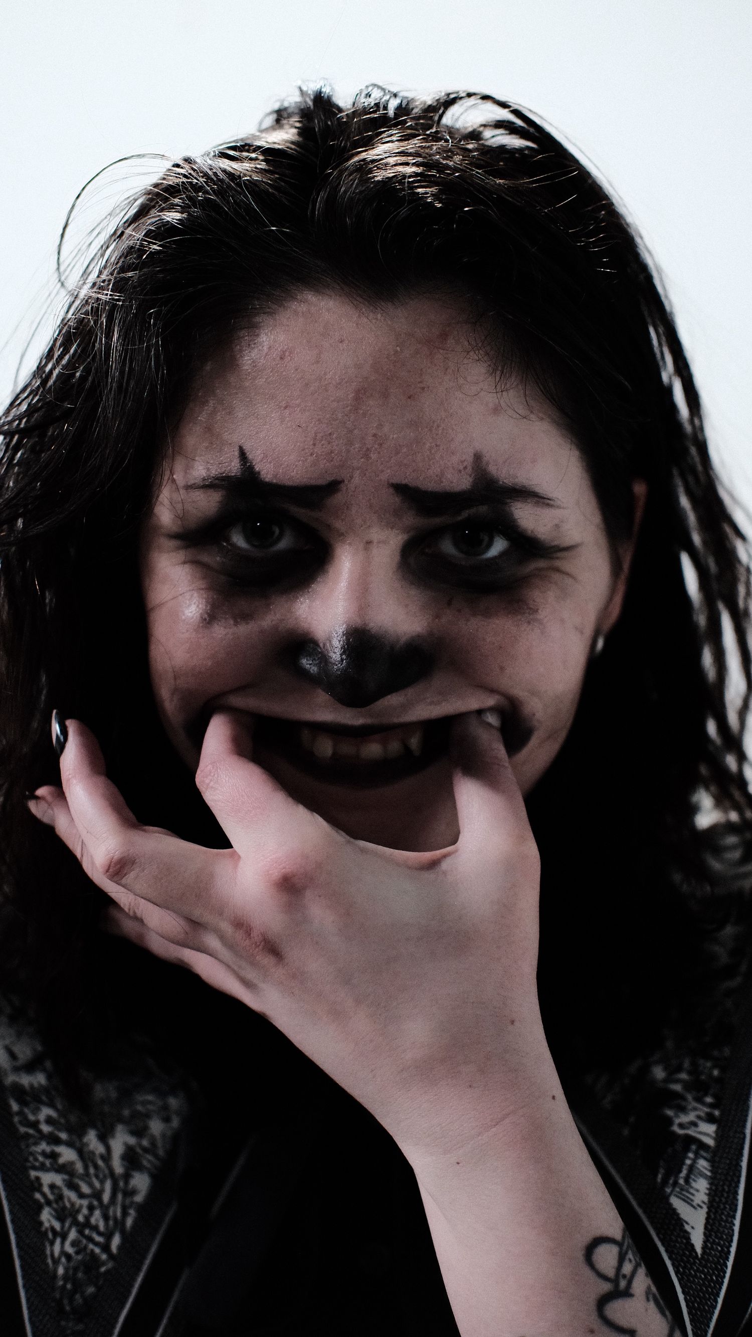 A dark and eerie portrait showing someone wearing dark makeup with hand covering their mouth in a haunting expression.