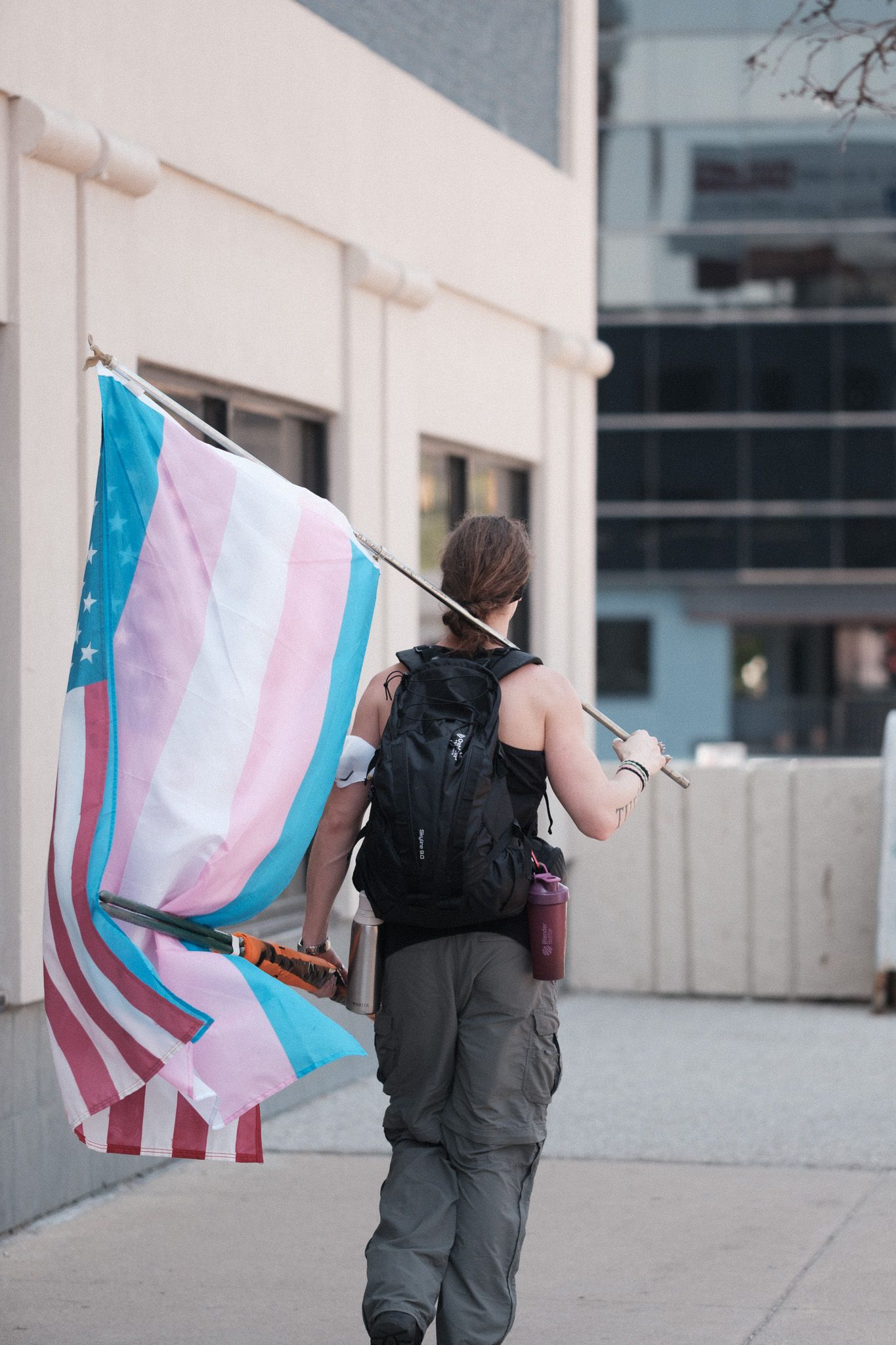 A person carrying a trans pride flag walks along a concrete plaza.
