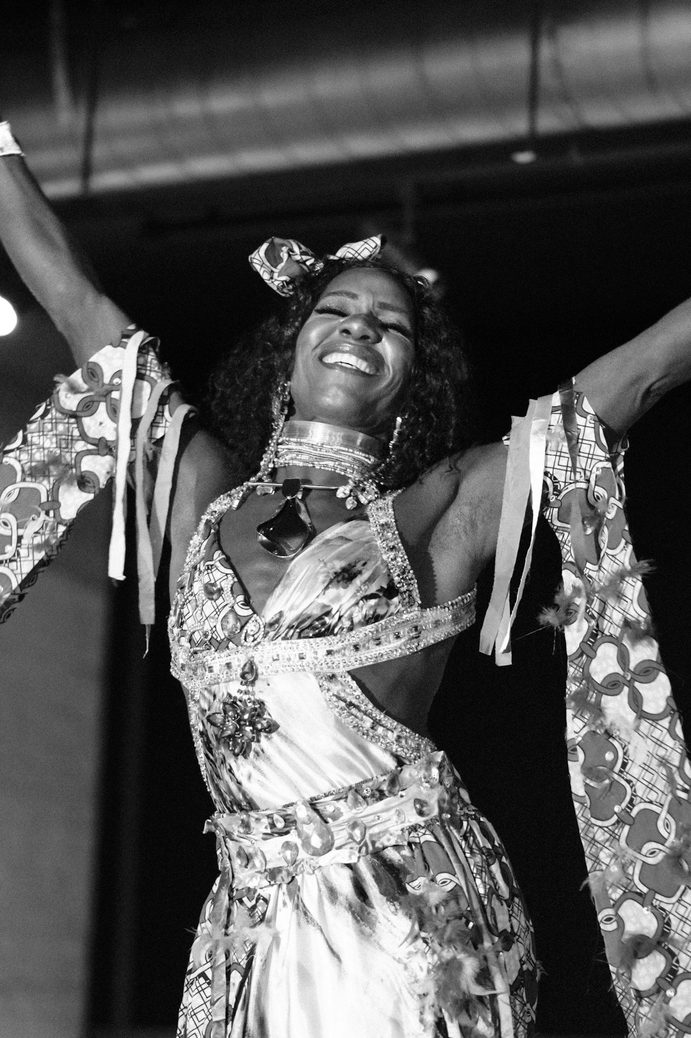 Joyful performer in white sequined costume with flowing sleeves raises arms triumphantly on stage.