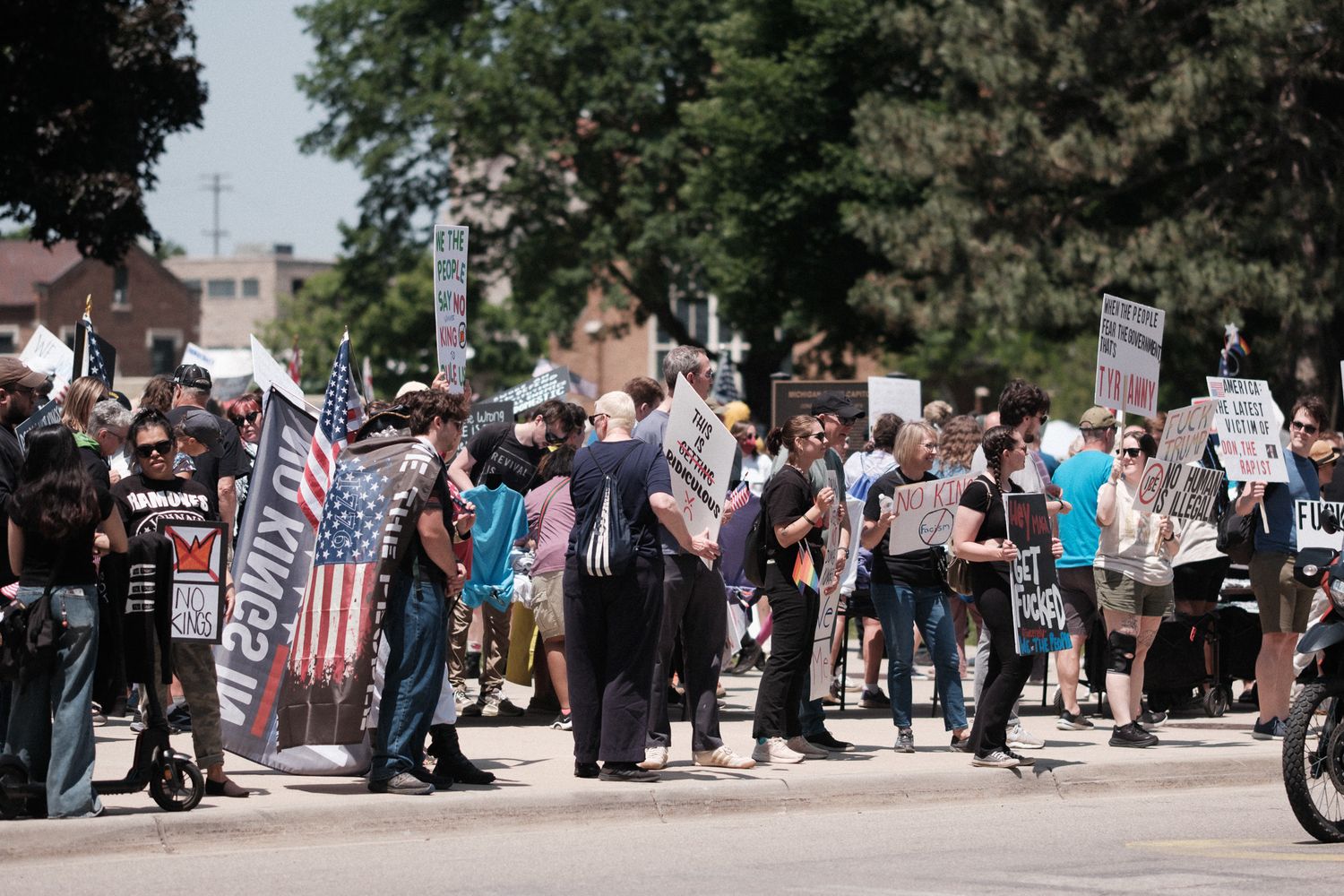 Protesters gather on a street with signs and flags during a demonstration.