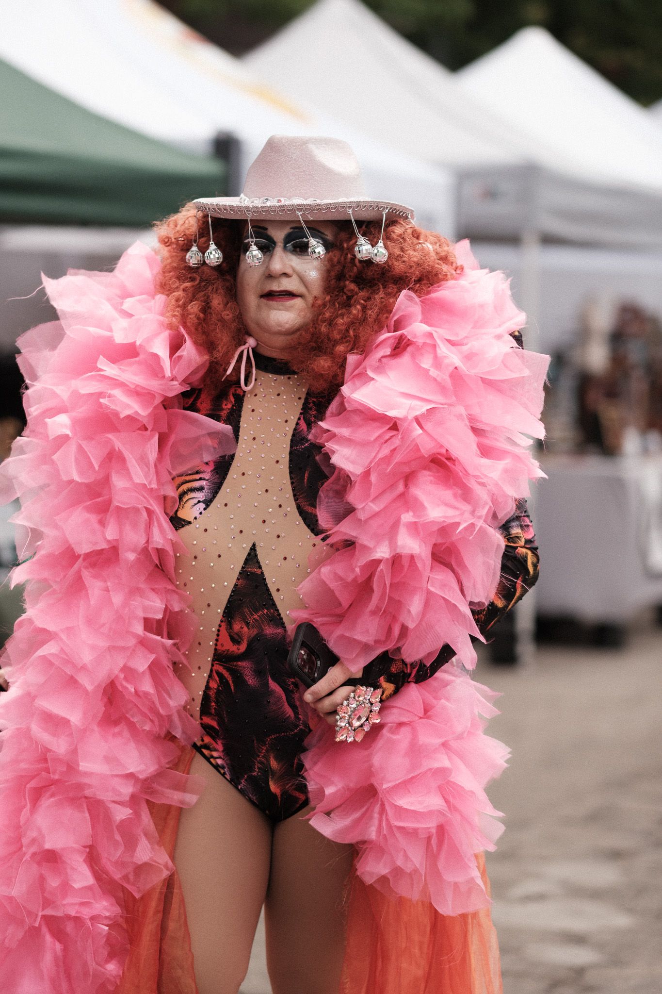 Person wearing black bodysuit with pink feather boa at outdoor festival.