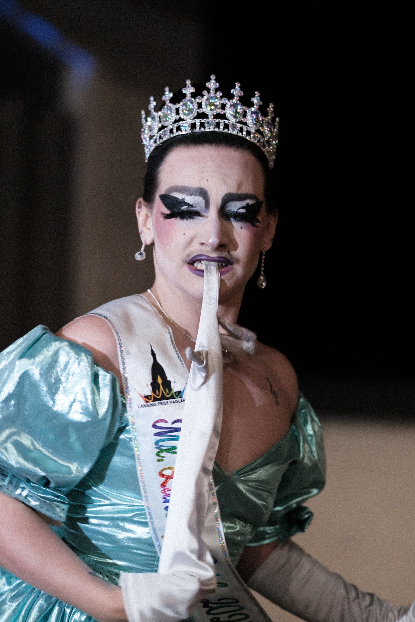 Dramatic stage performer wearing a silver crown and mint green gown with theatrical makeup.