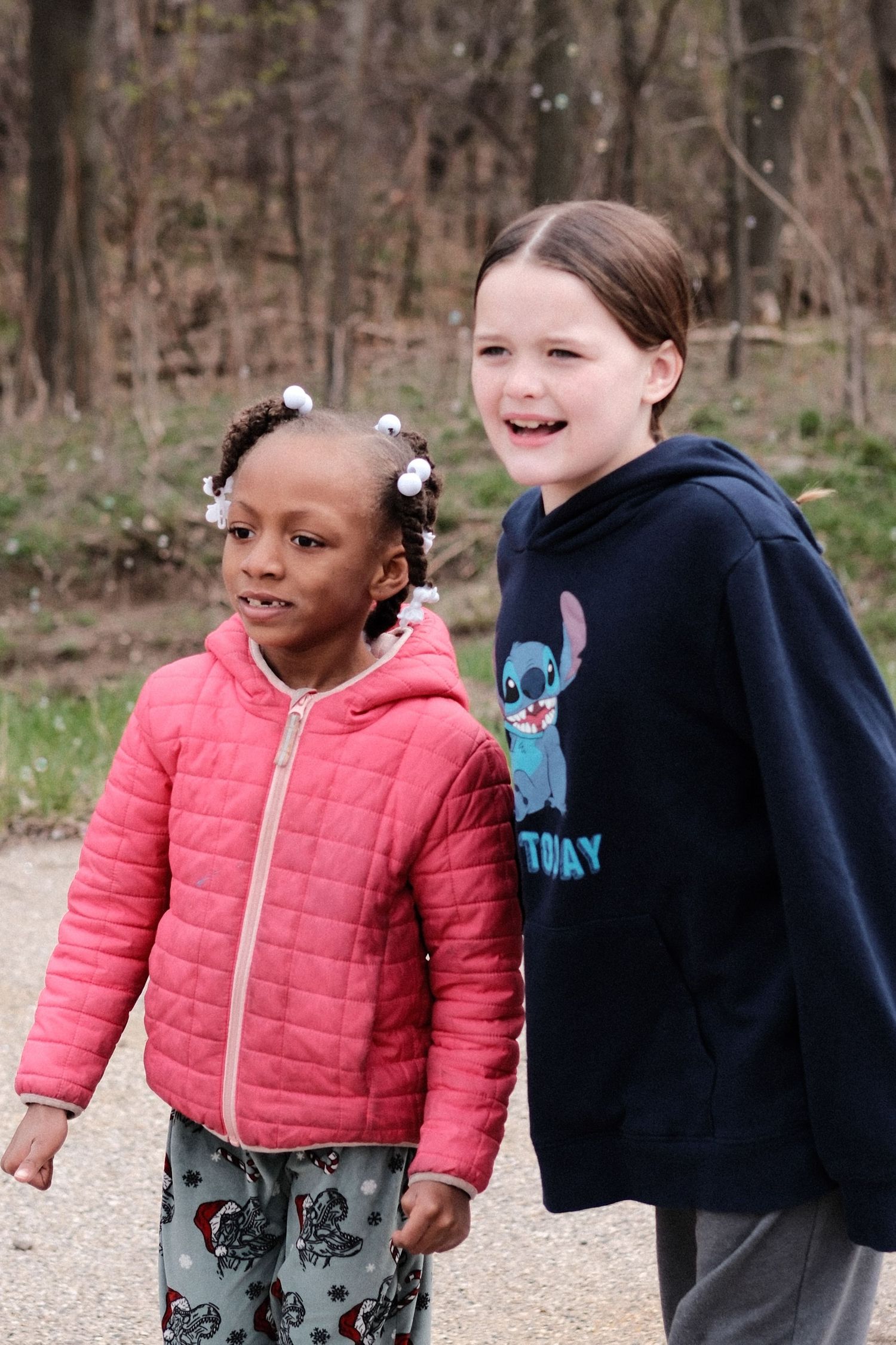 Two young friends in winter coats share a happy moment together on a wooded path.