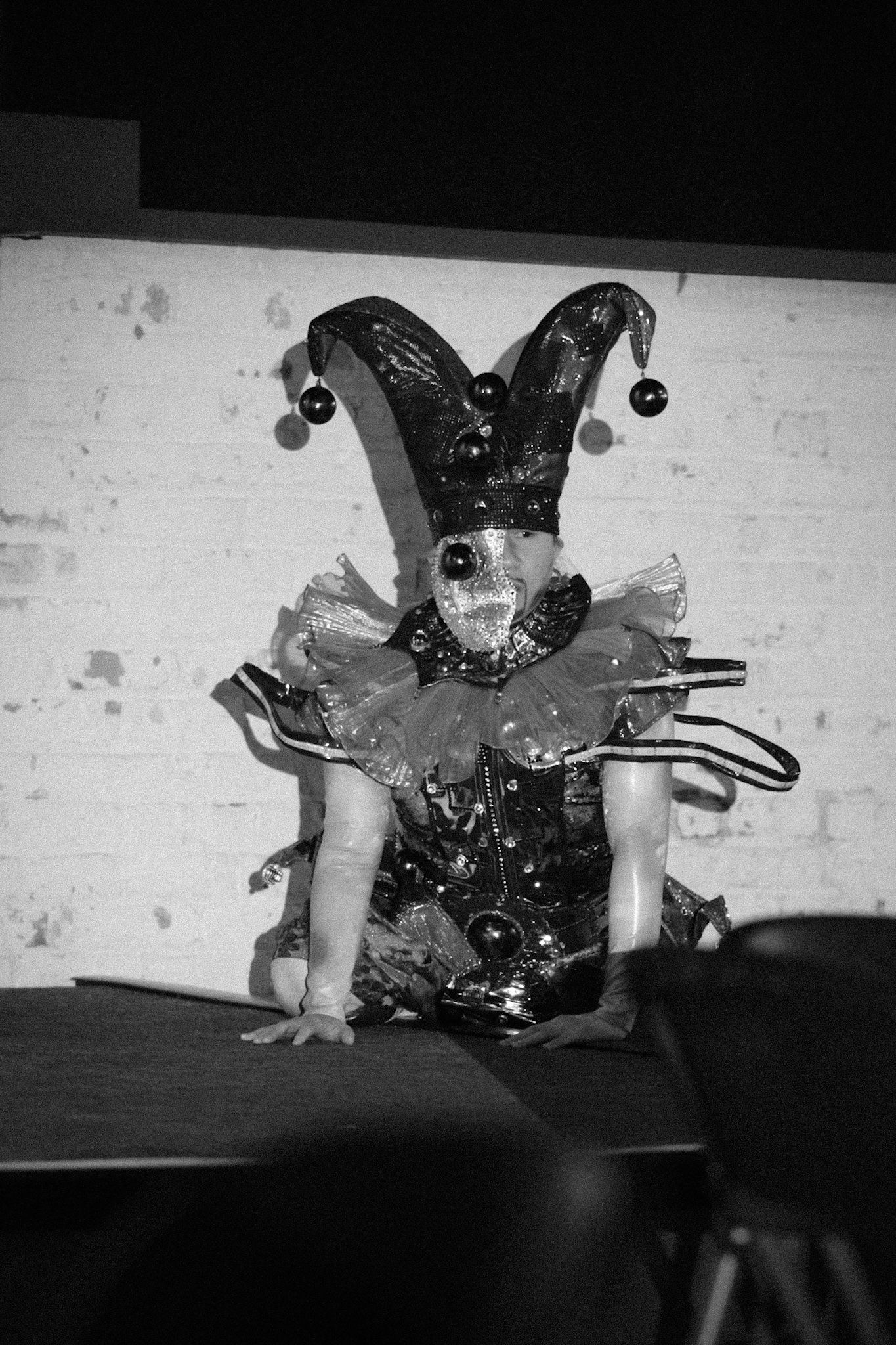 Performer in black and white jester costume with bells during theatrical show.