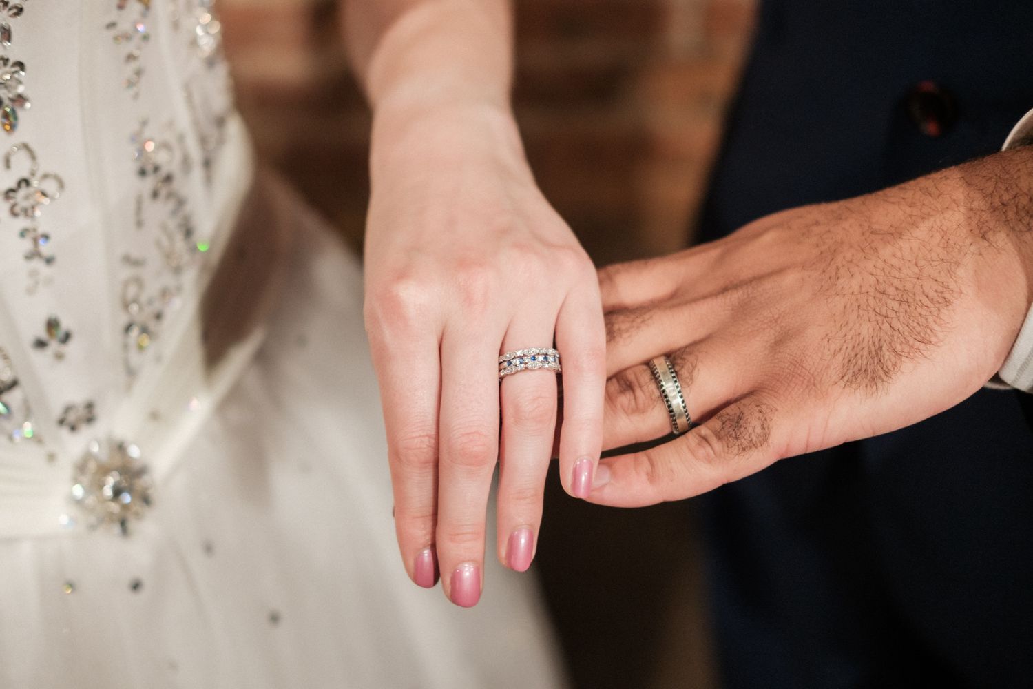 Close-up view of two hands wearing wedding rings against a blurred background.