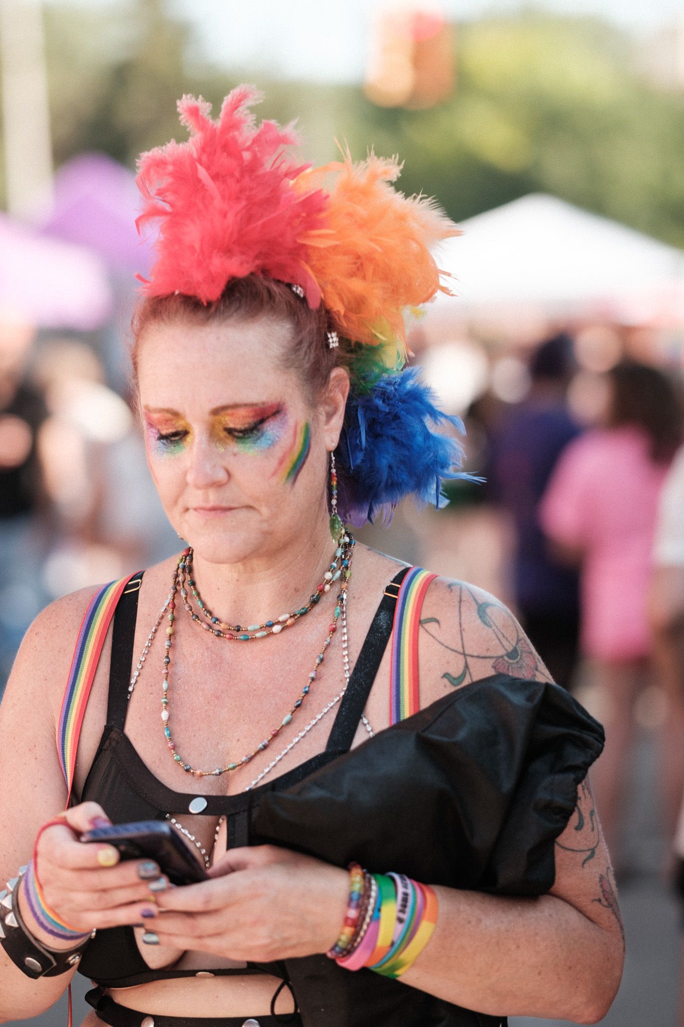 Person with colorful hair and festival attire checking their phone at an outdoor event with crowd in background.