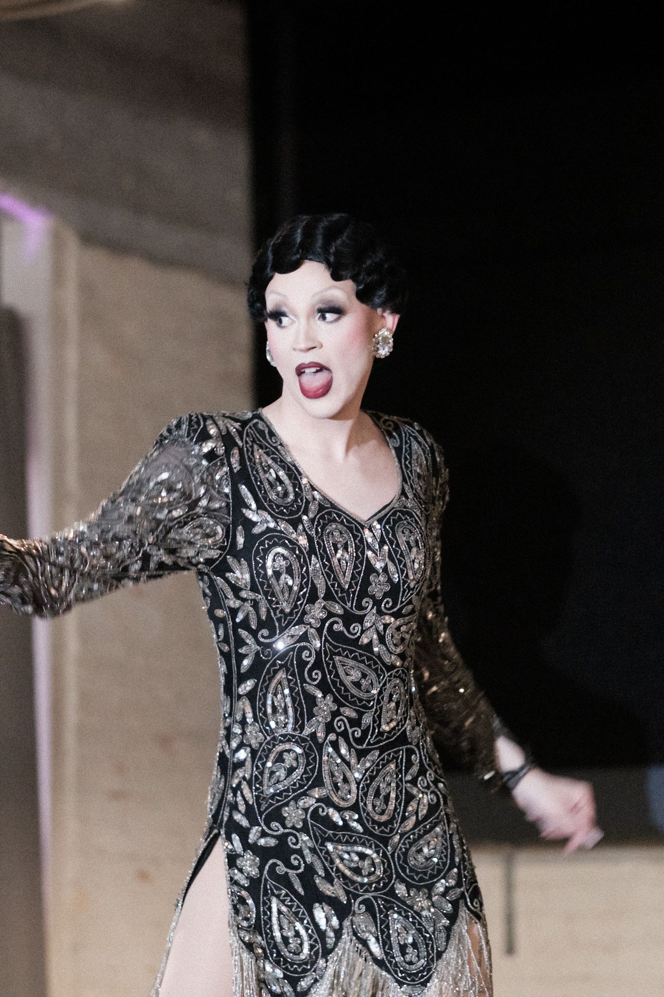 Performer in sparkling black dress striking dramatic pose on stage.