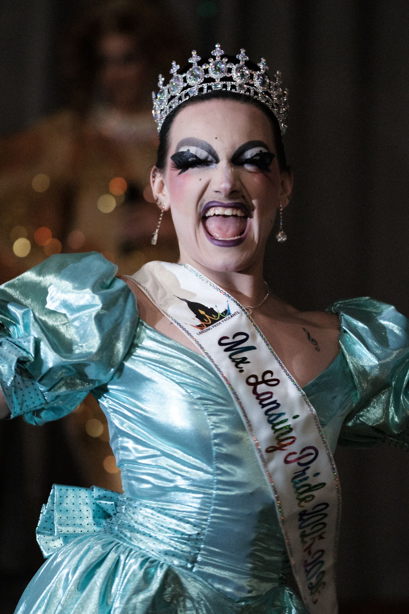 Pageant contestant in aqua ballgown and crown displays joyful expression during competition.