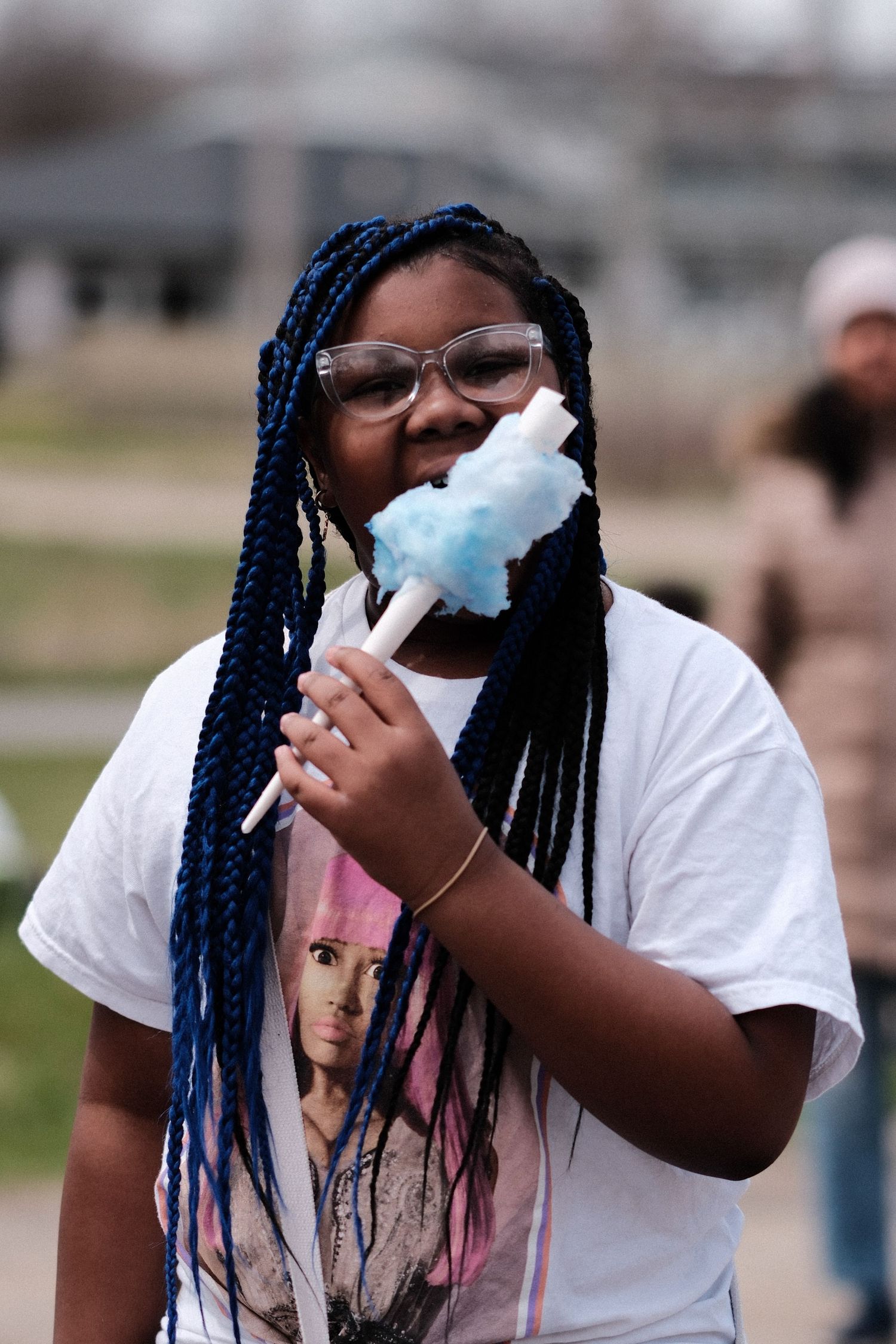 Person with blue braids wearing white t-shirt and face mask outdoors.