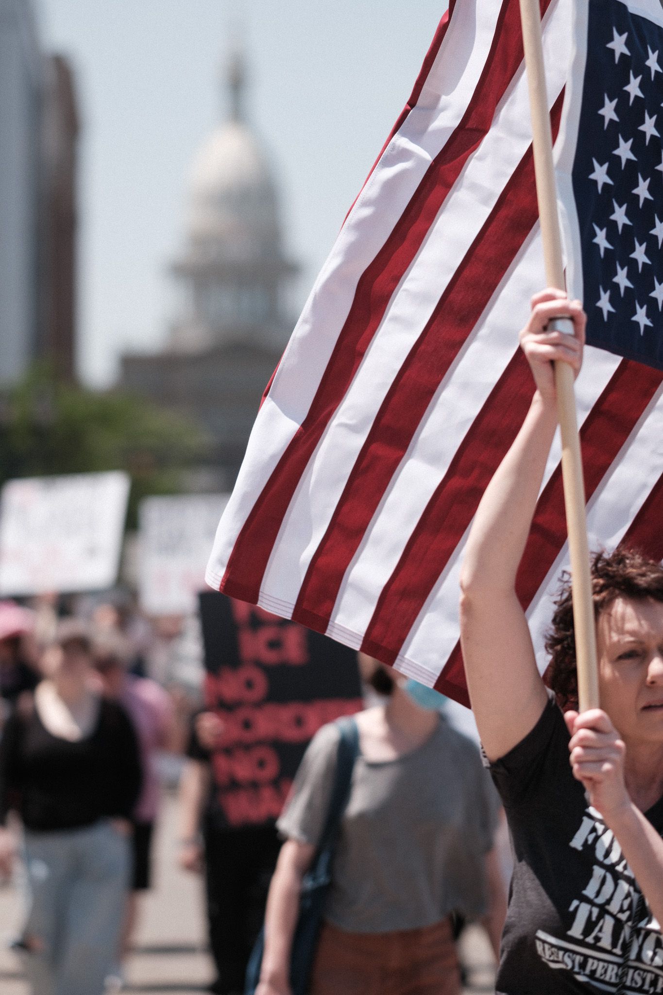 American flag being held up during protest with state capitol building visible in background.