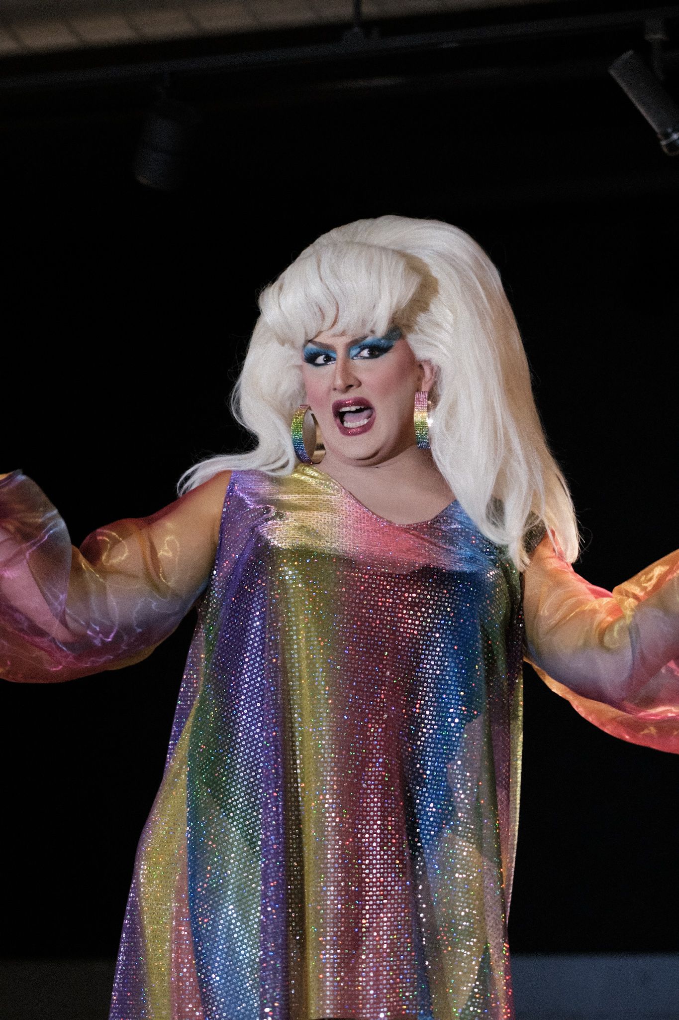Performer in shimmering rainbow dress performing under stage lights.