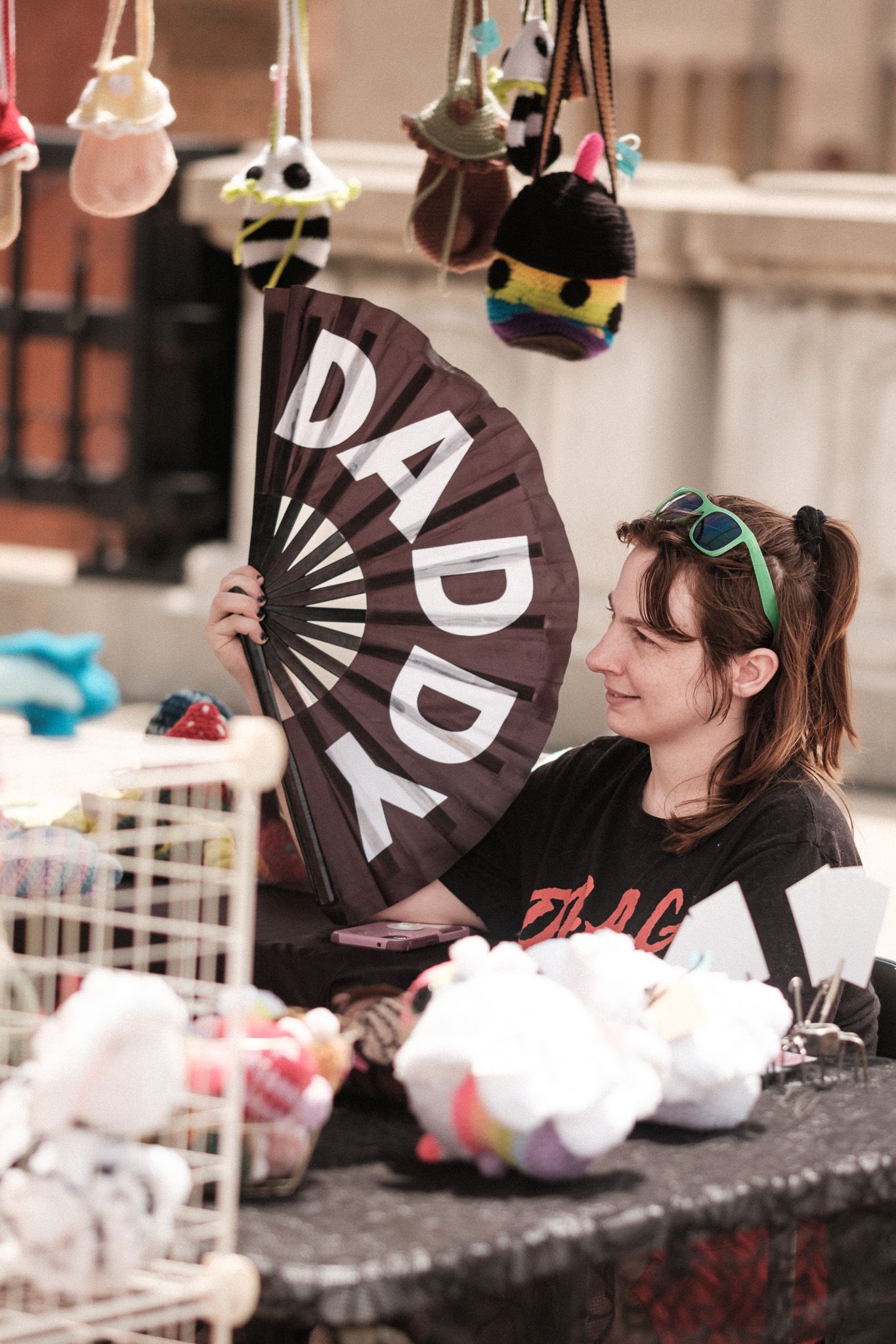 A black folding fan with DADDY text is displayed at a vendor booth with hanging decorations.