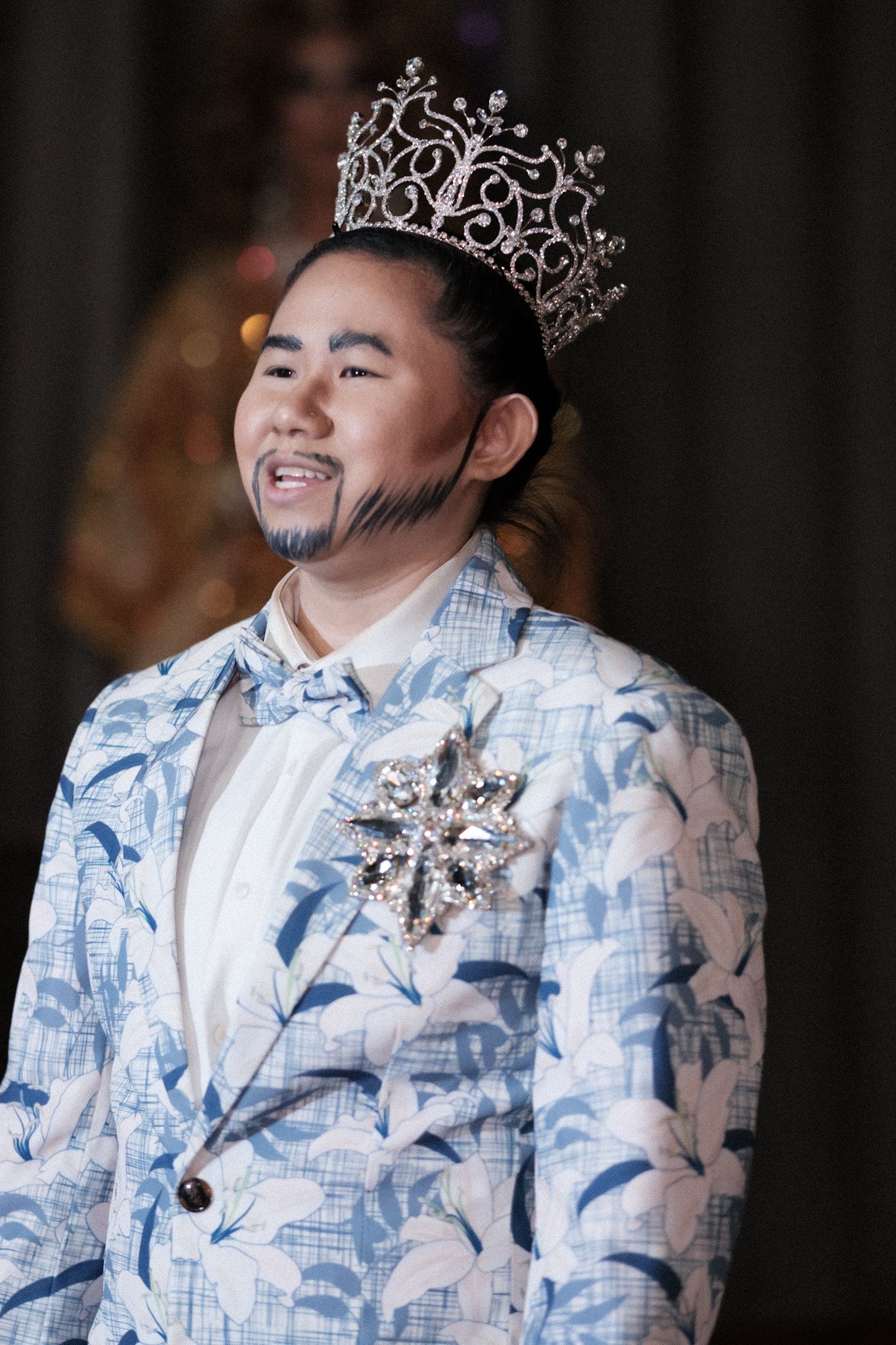 Performer in blue and white floral suit jacket wearing ornate silver crown.