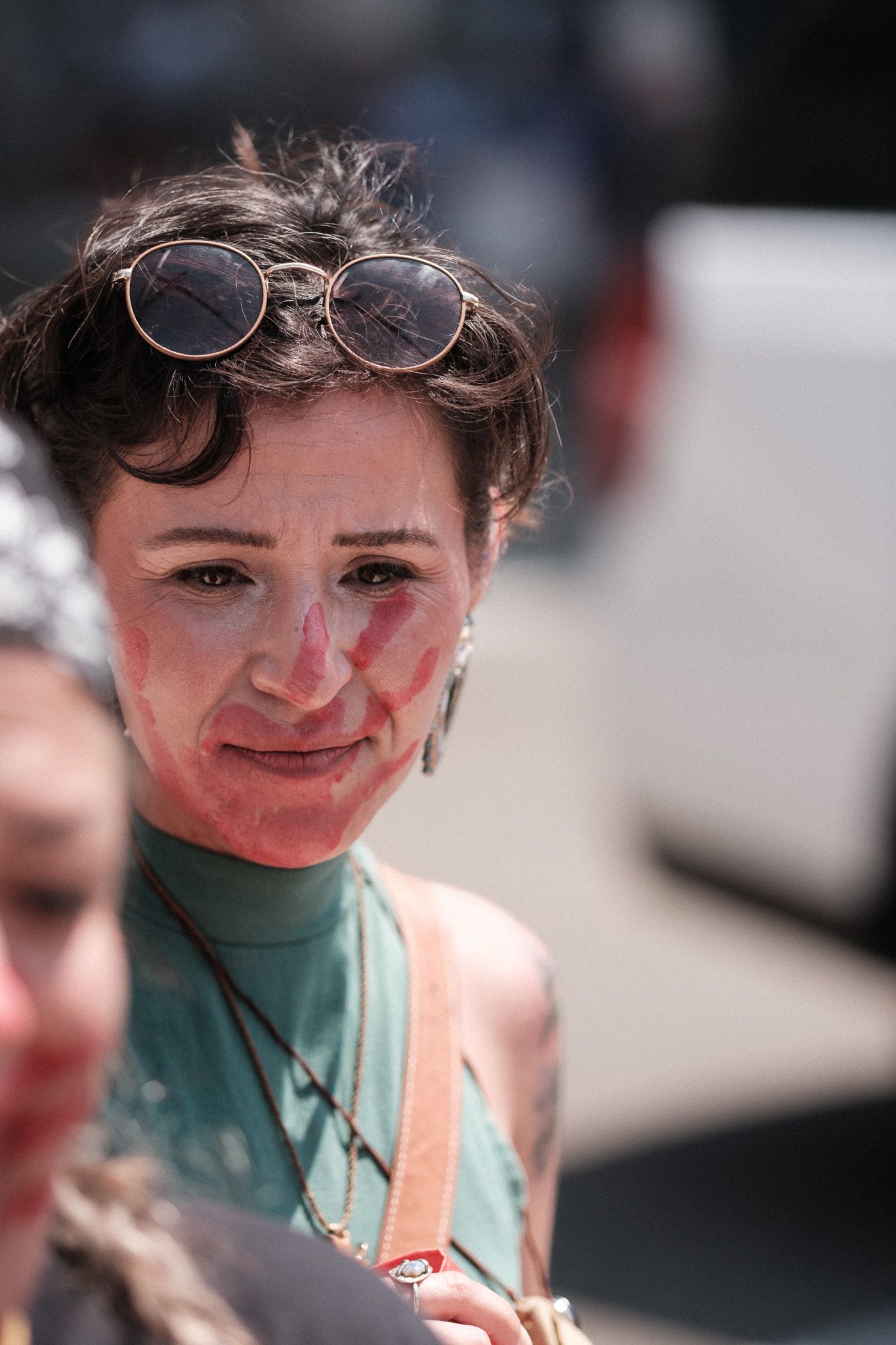 Person wearing glasses and green top smiles with face paint at an outdoor gathering.