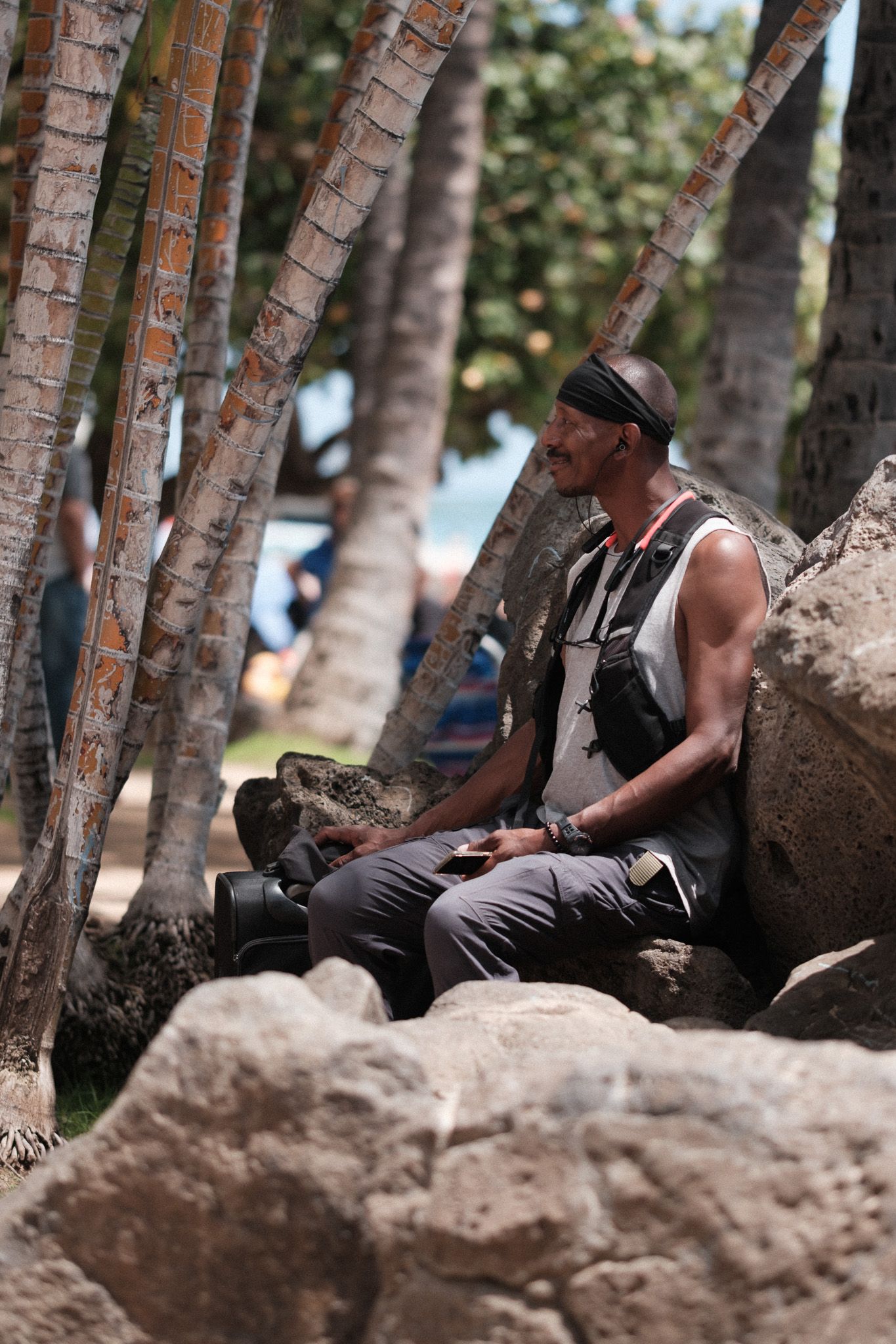 A person rests on large rocks beneath palm trees at a tropical location while wearing casual hiking attire.