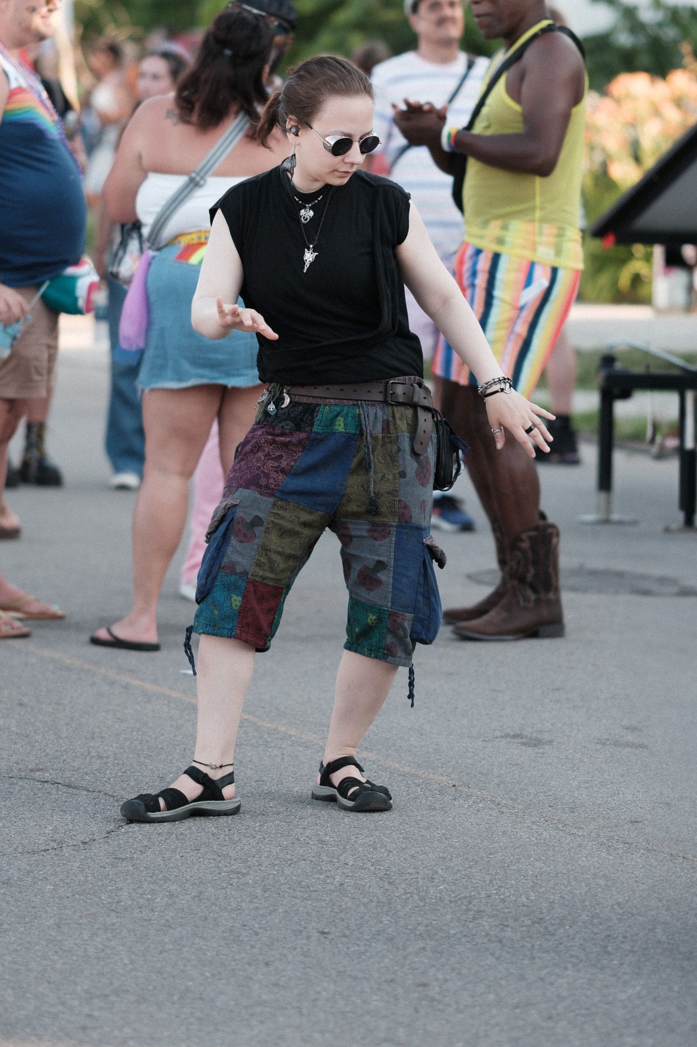 Person dancing in patchwork shorts and black top at an outdoor festival.