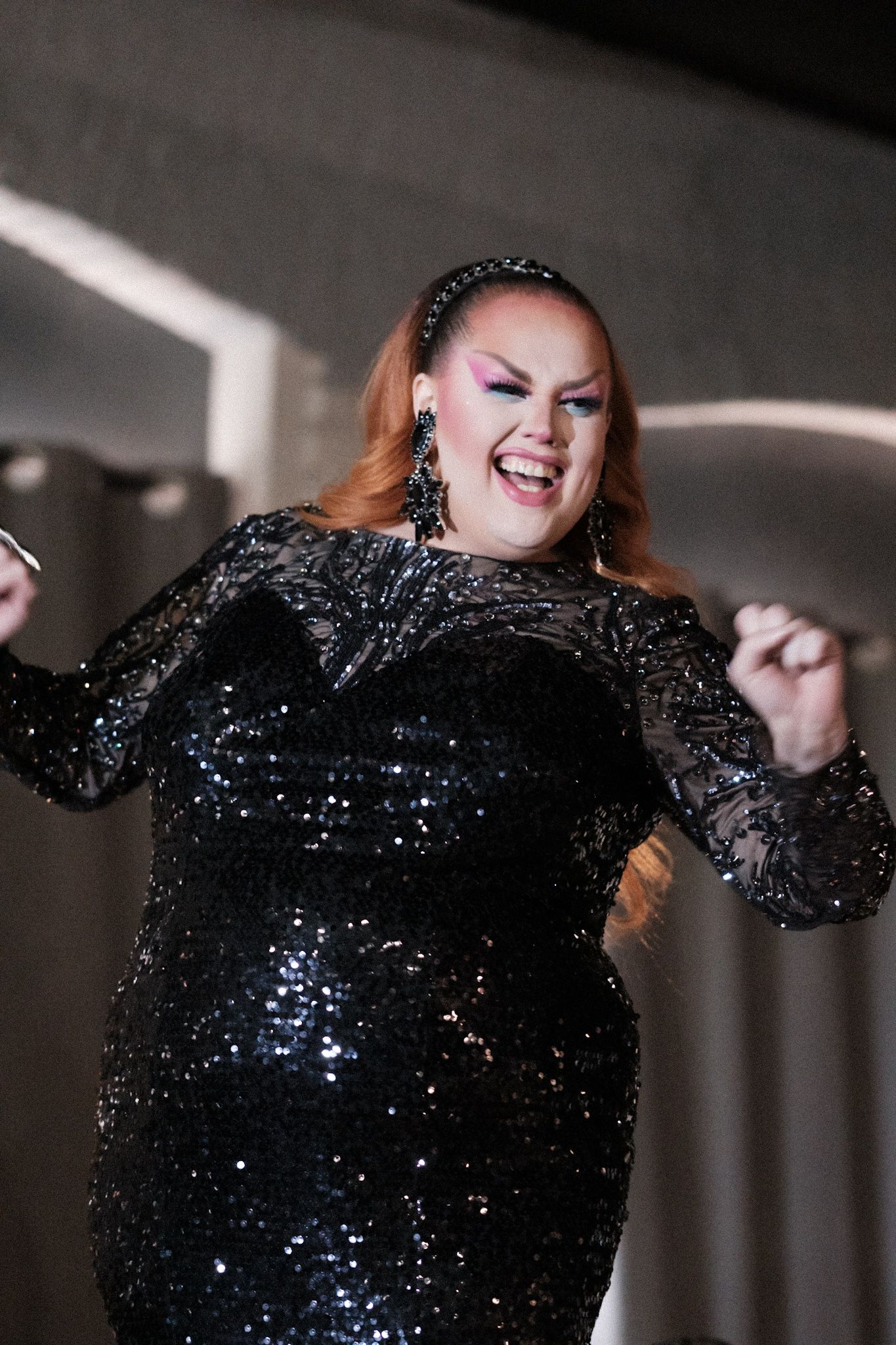 Joyful performer in sparkling black sequined dress dancing on stage.