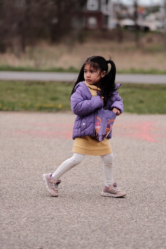 Child in purple jacket and light pants running and playing on a concrete surface.